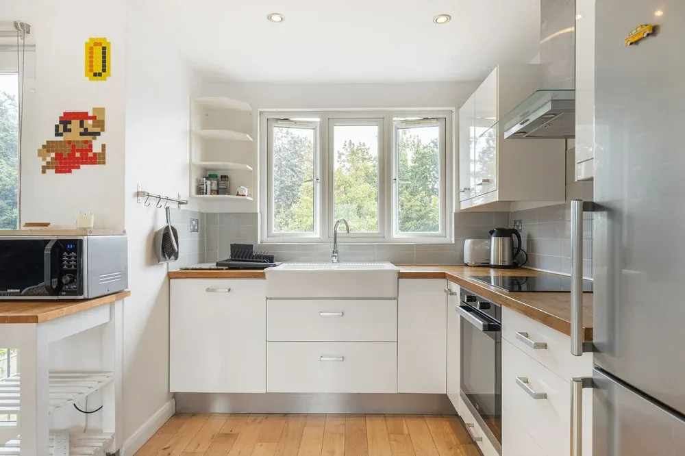 A bright modern kitchen with white cabinets, wood countertops, and a central sink.