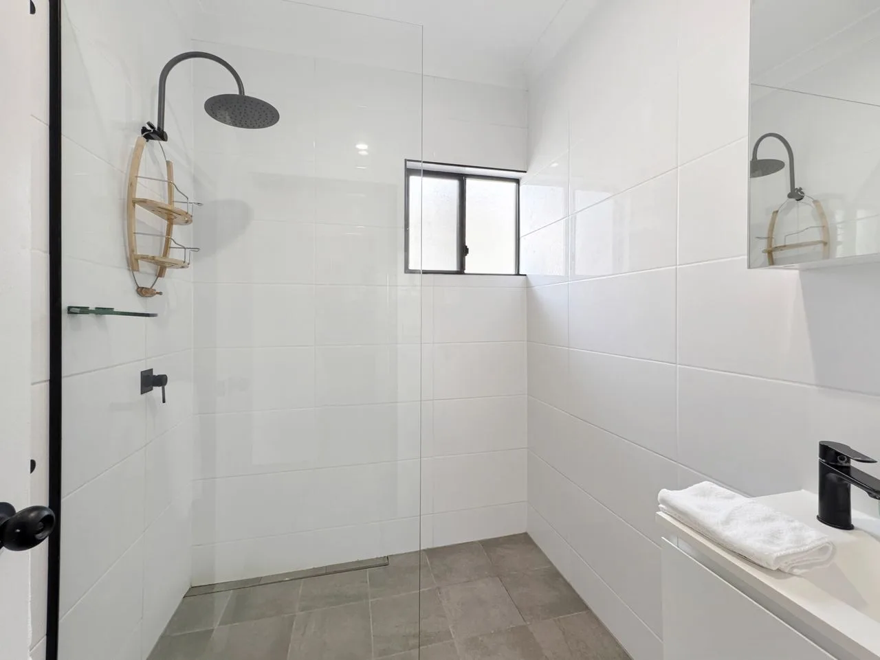 A tiled bathroom with a glass shower and a small window.