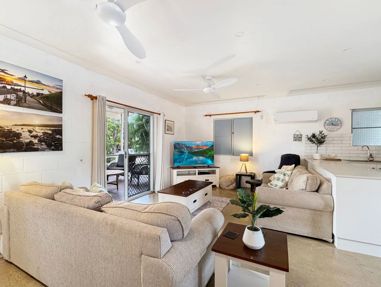 A bright living room with seating, a television, and a compact kitchen area.