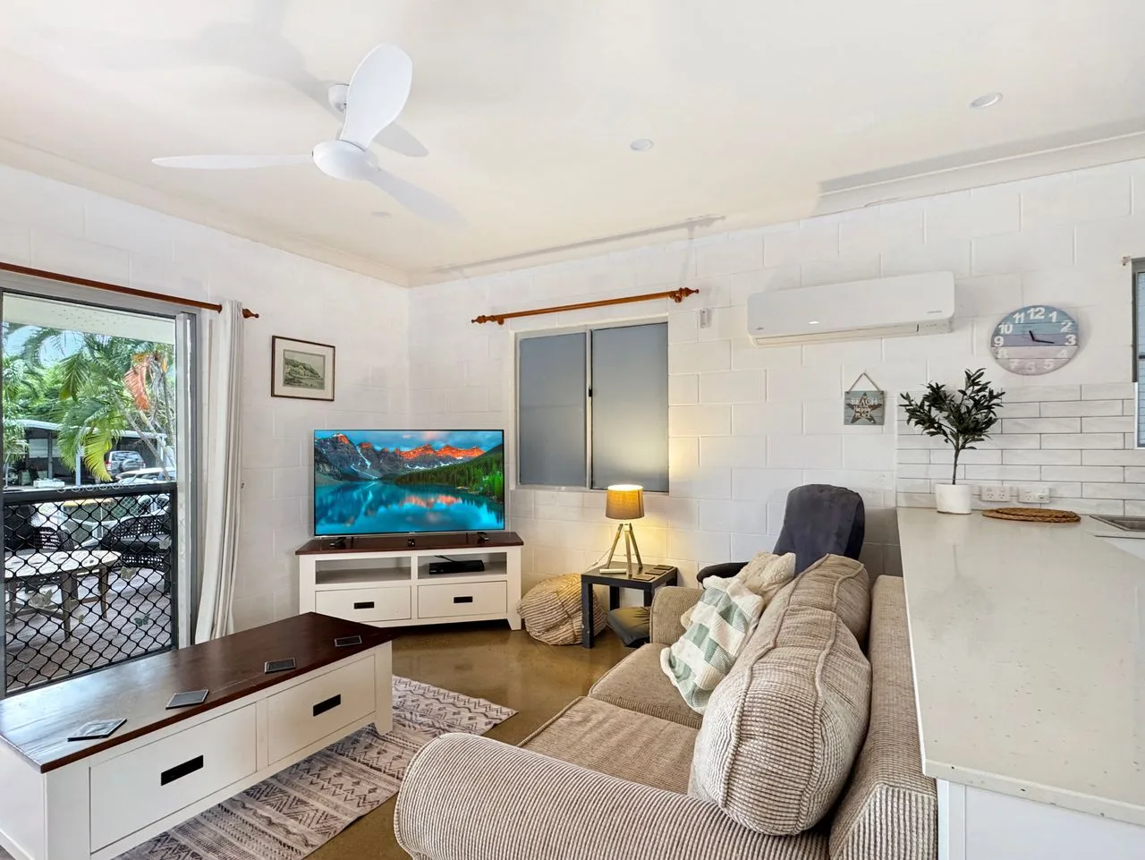 A bright living room with seating, a television, and sliding windows.