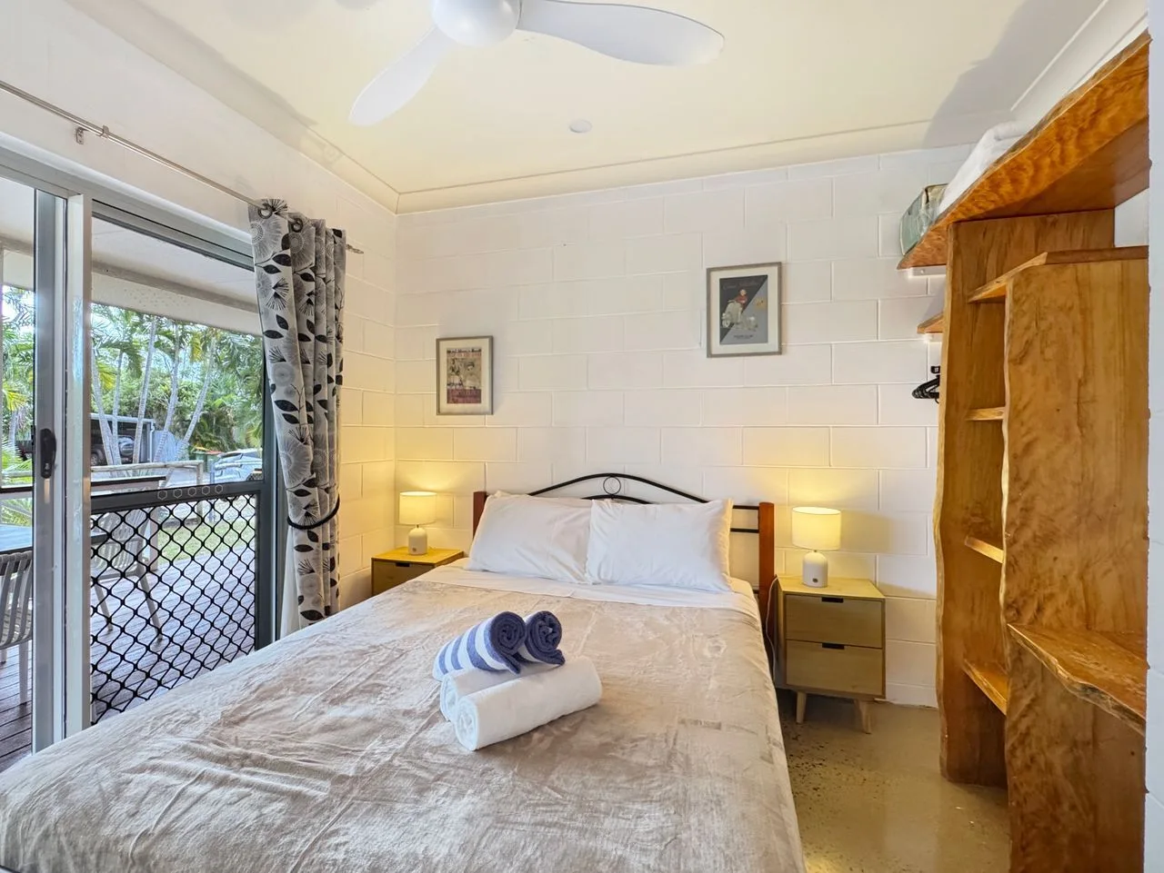 A bedroom with a neatly made bed, bedside tables, and a glass door opening to a patio.
