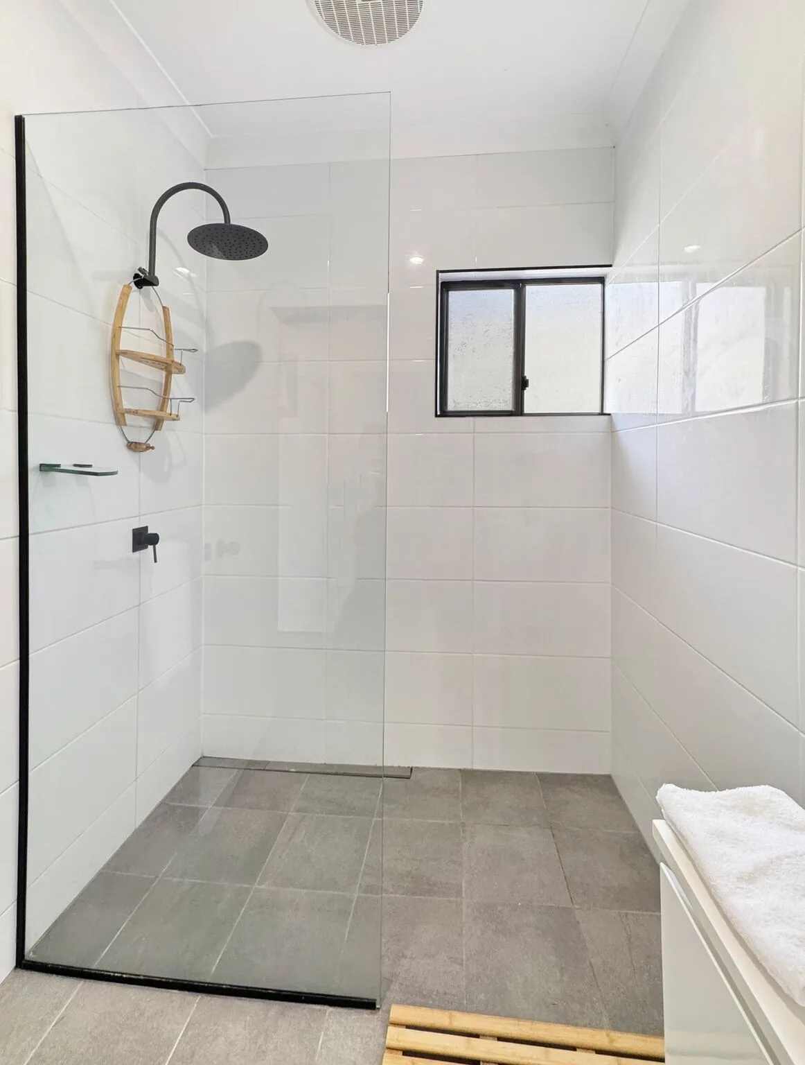 A tiled bathroom with a glass shower screen and a small window.