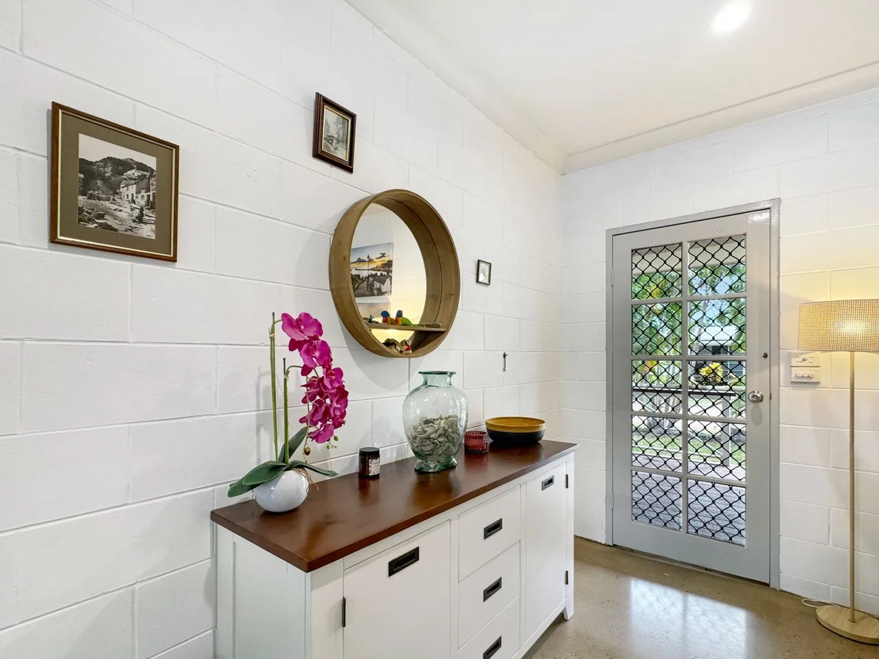 A bright entryway with a white cabinet, round mirror, and glass-paned door.