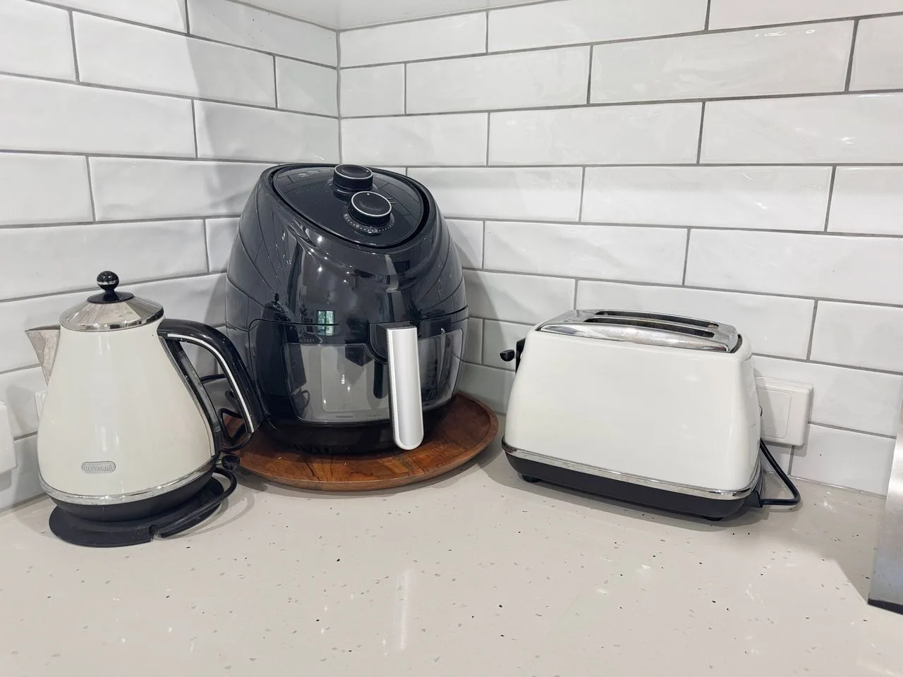 A kitchen counter holds a kettle, air fryer, and toaster against a tiled wall.
