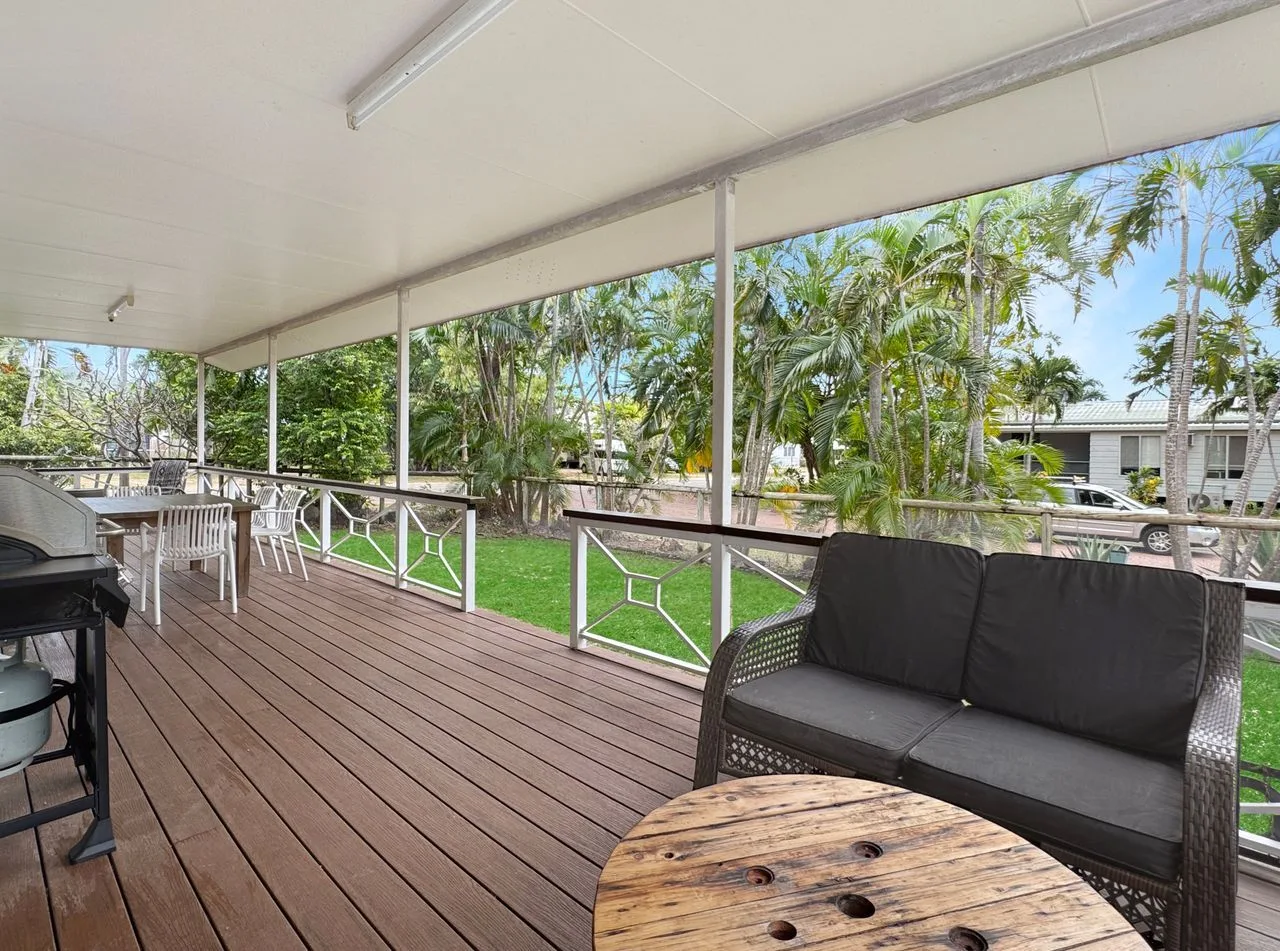 A covered outdoor deck has seating overlooking a green garden.