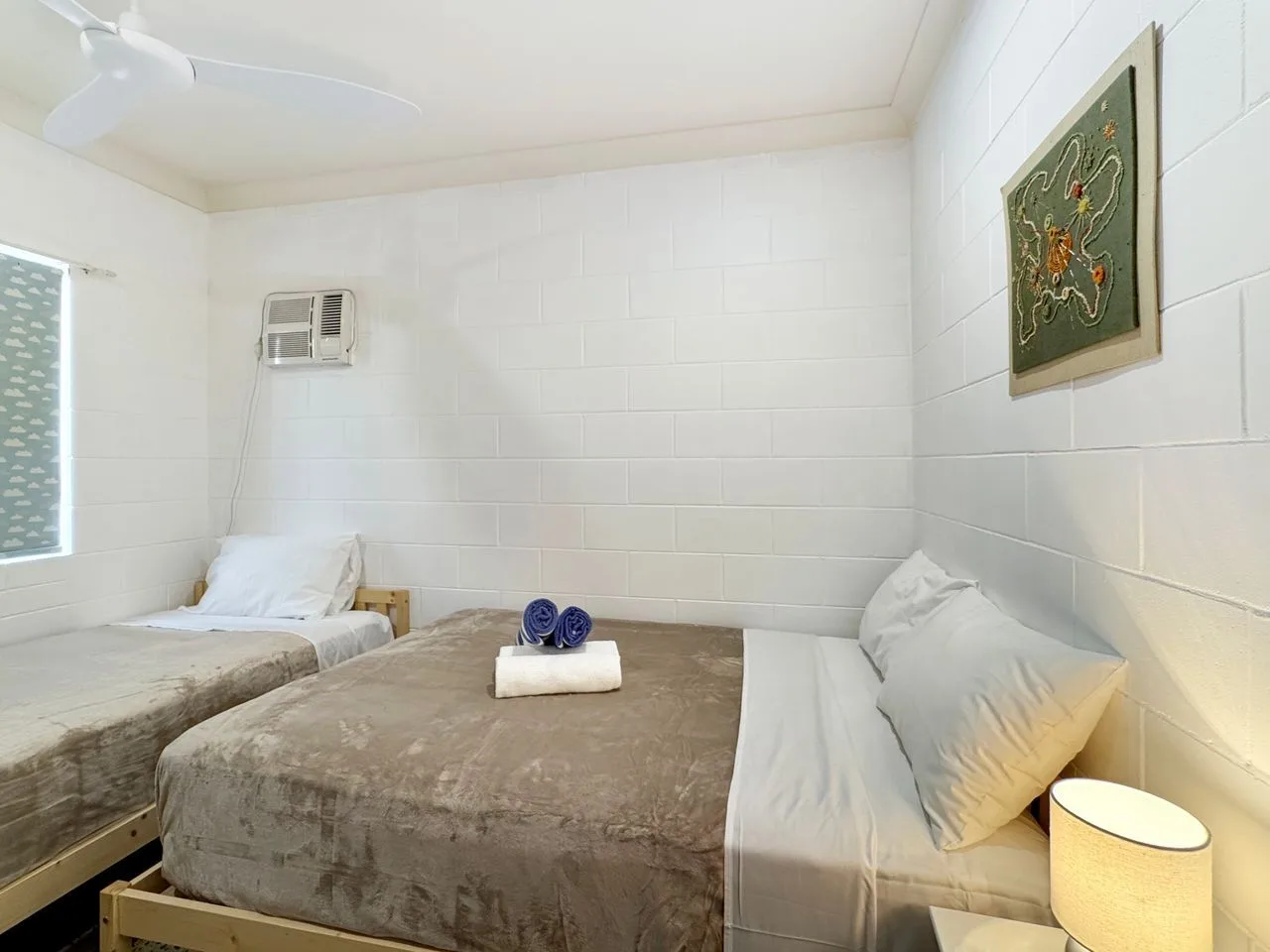 A bedroom with two beds and folded towels on the center bed.