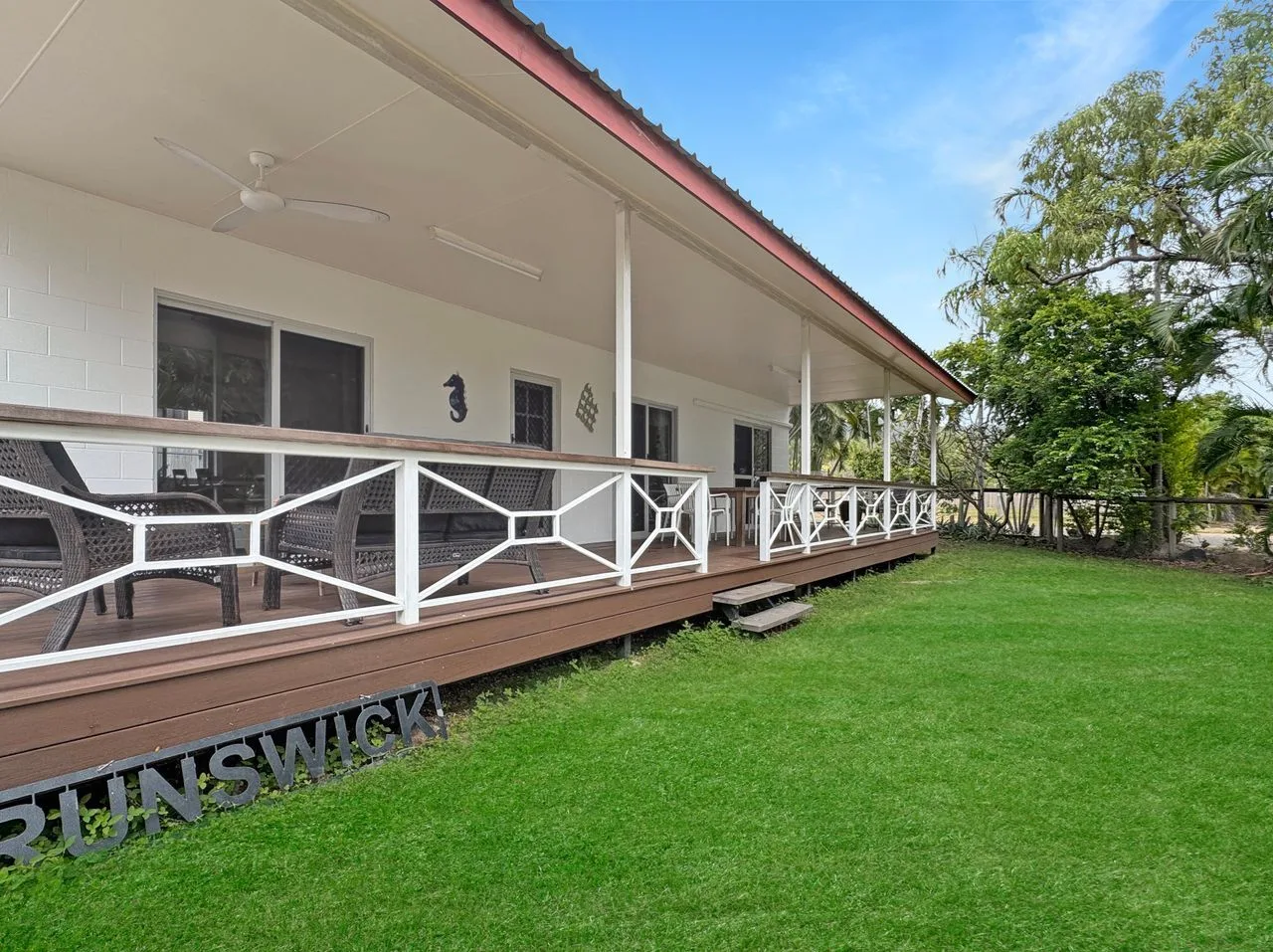 A long covered veranda with white railings overlooks a grassy lawn.