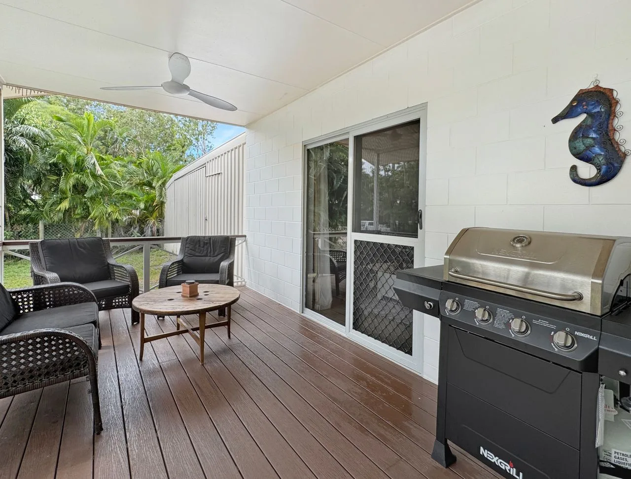 A covered deck has outdoor seating, a coffee table, and a barbecue grill.