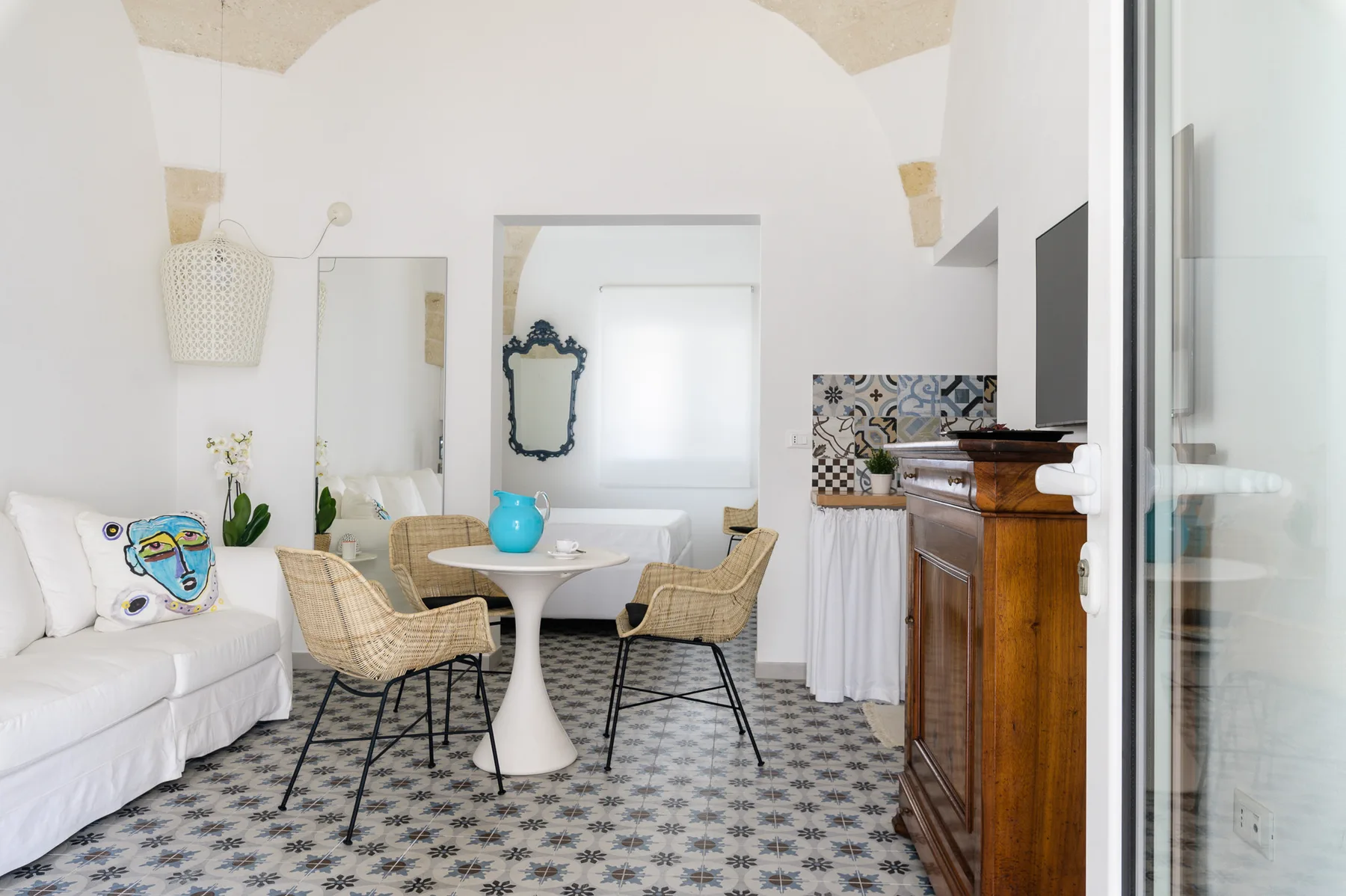 Una luminosa zona de comedor y estar con una mesa redonda, asientos tejidos y un sofá blanco.