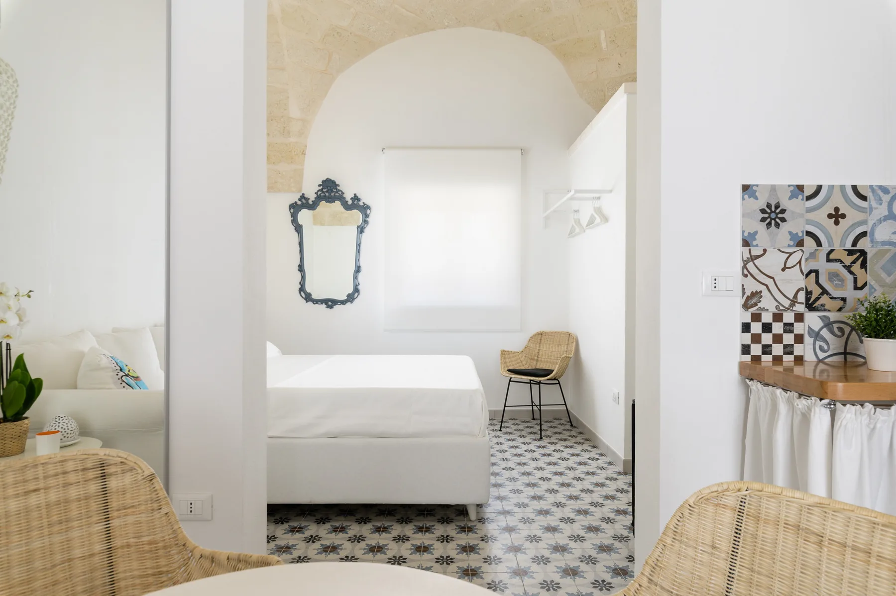 Un dormitorio con una cama blanca, un espejo decorativo y suelo de baldosas estampadas.