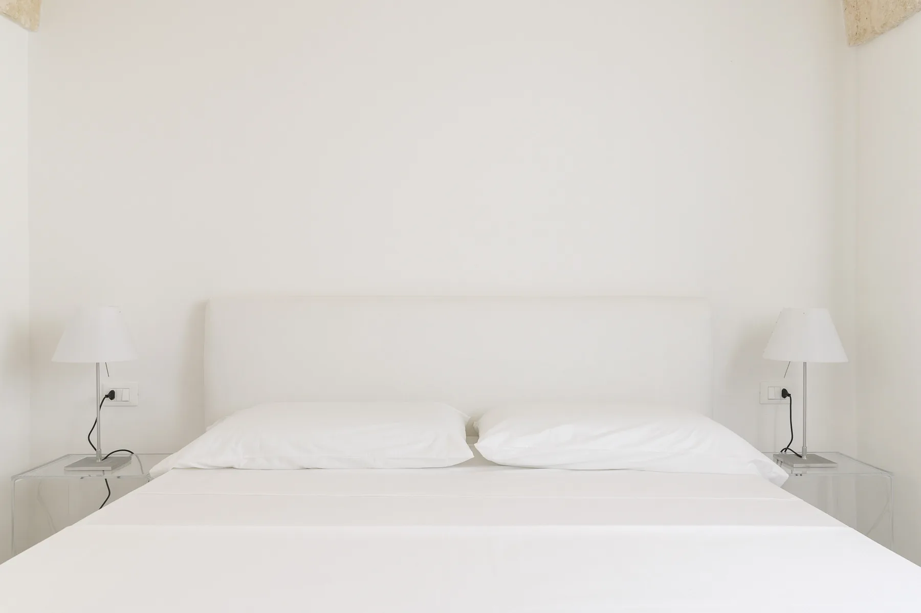 Un dormitorio luminoso con una cama bien tendida y lámparas junto a la cama.
