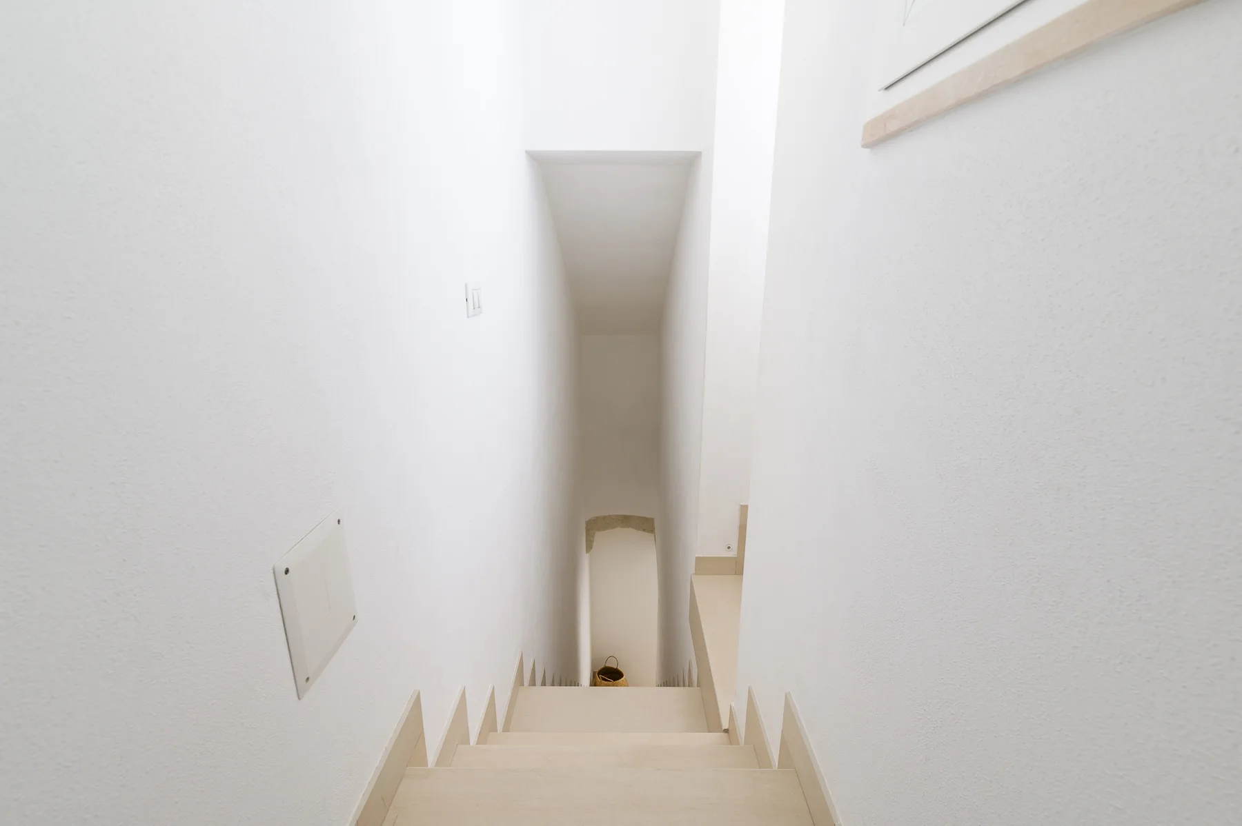 Una escalera interior estrecha desciende entre paredes blancas.