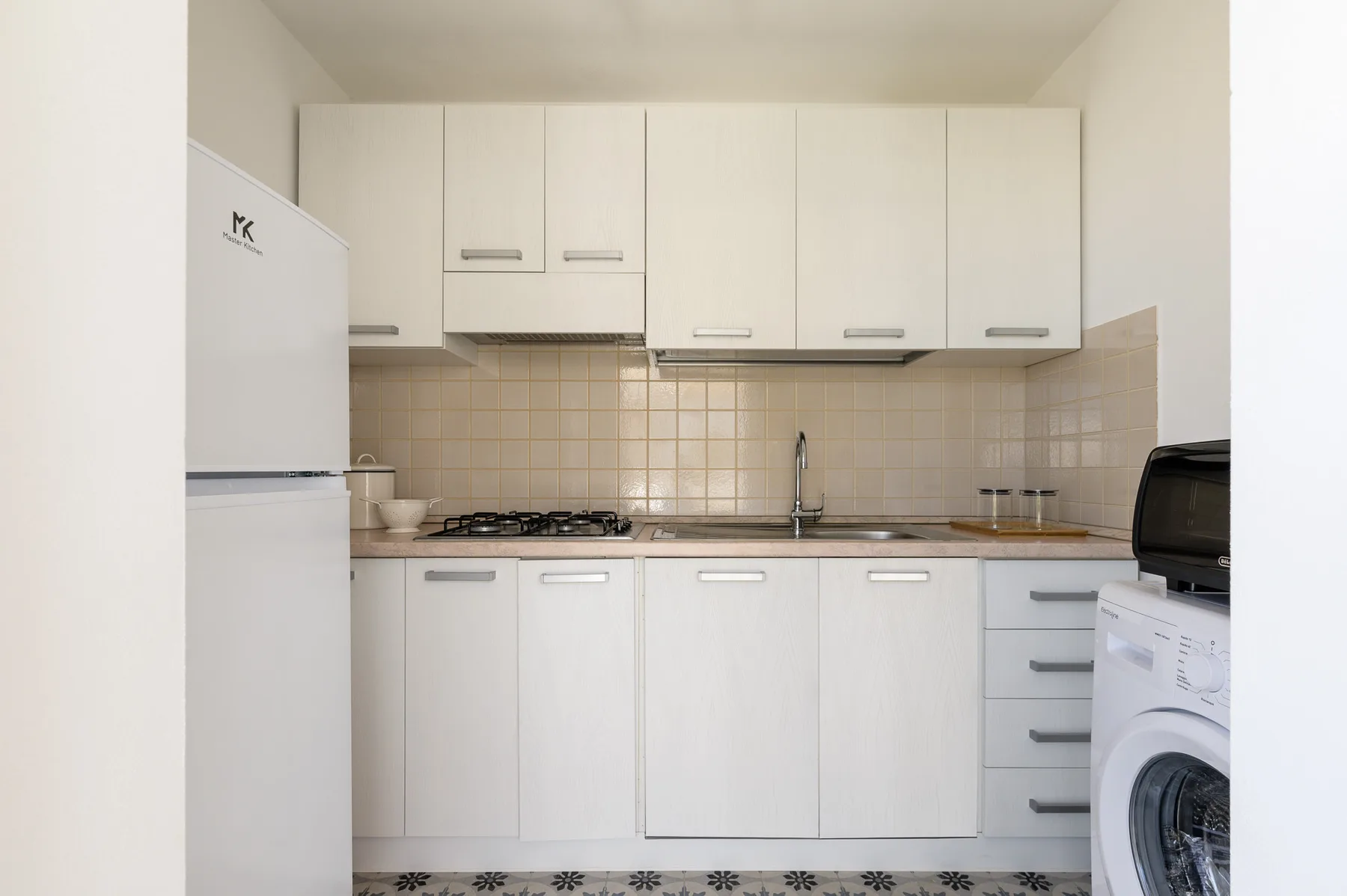 Una cocina compacta con armarios blancos, una encimera y una lavadora.