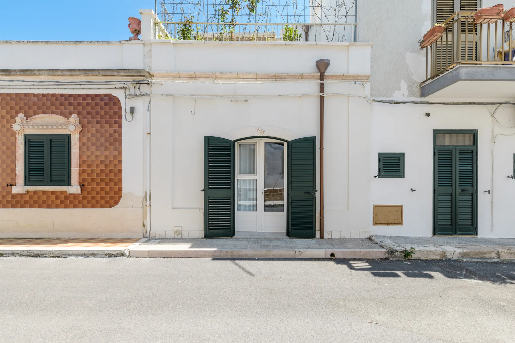 Fachada de un edificio blanco con contraventanas verde oscuro y una puerta central.