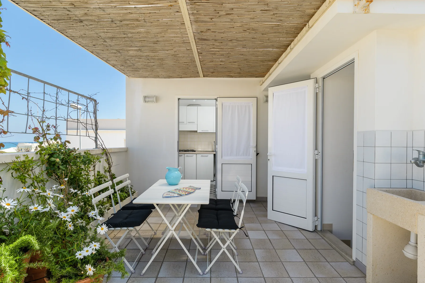 Una zona cubierta para comer al aire libre, con mesa y sillas junto a una puerta abierta.