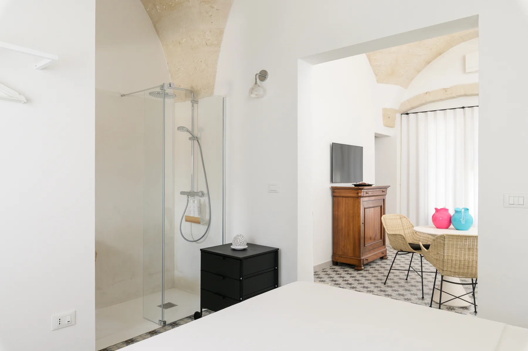 Un dormitorio luminoso se abre a una zona de estar, con una ducha de vidrio al lado.