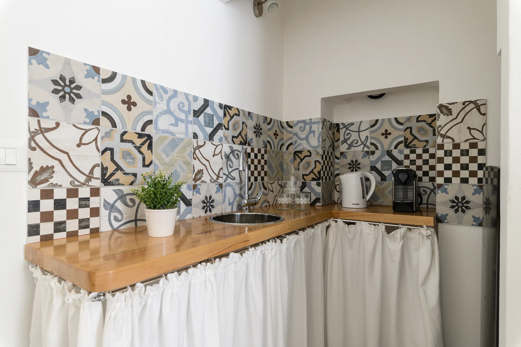 Una cocina compacta con encimera de madera, azulejos estampados y pequeños electrodomésticos.