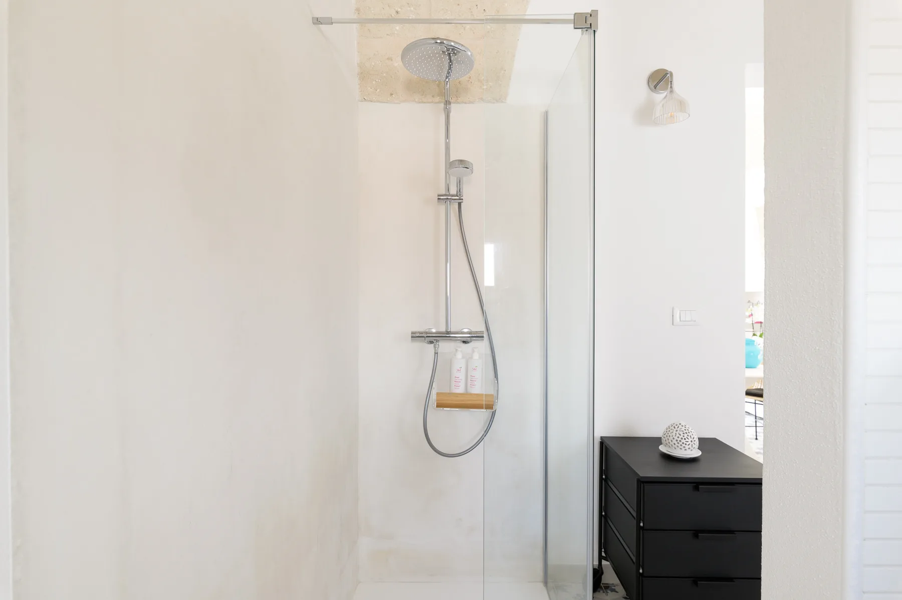 Un baño luminoso con una ducha de vidrio y un mueble oscuro.