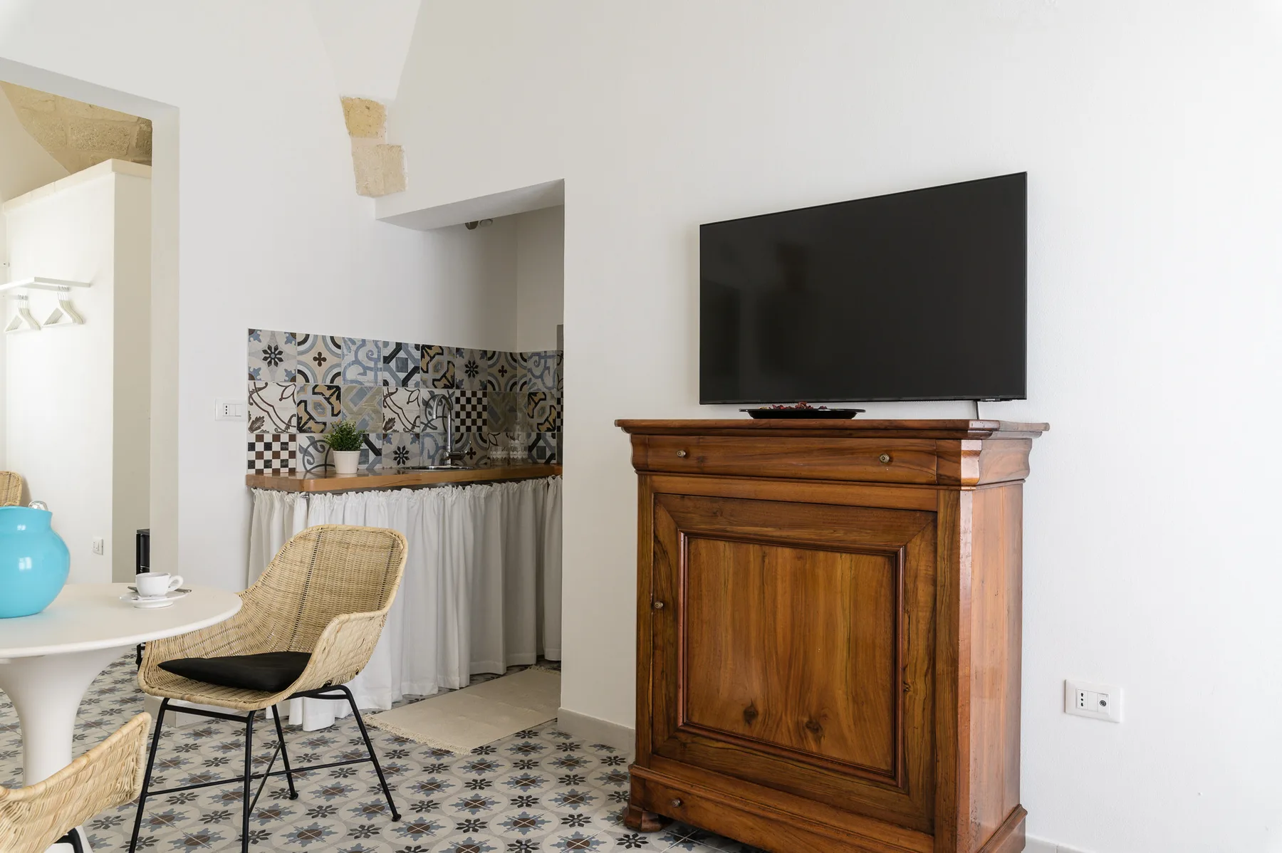 Una sala de estar con un televisor sobre un mueble de madera junto a una pequeña mesa de comedor.