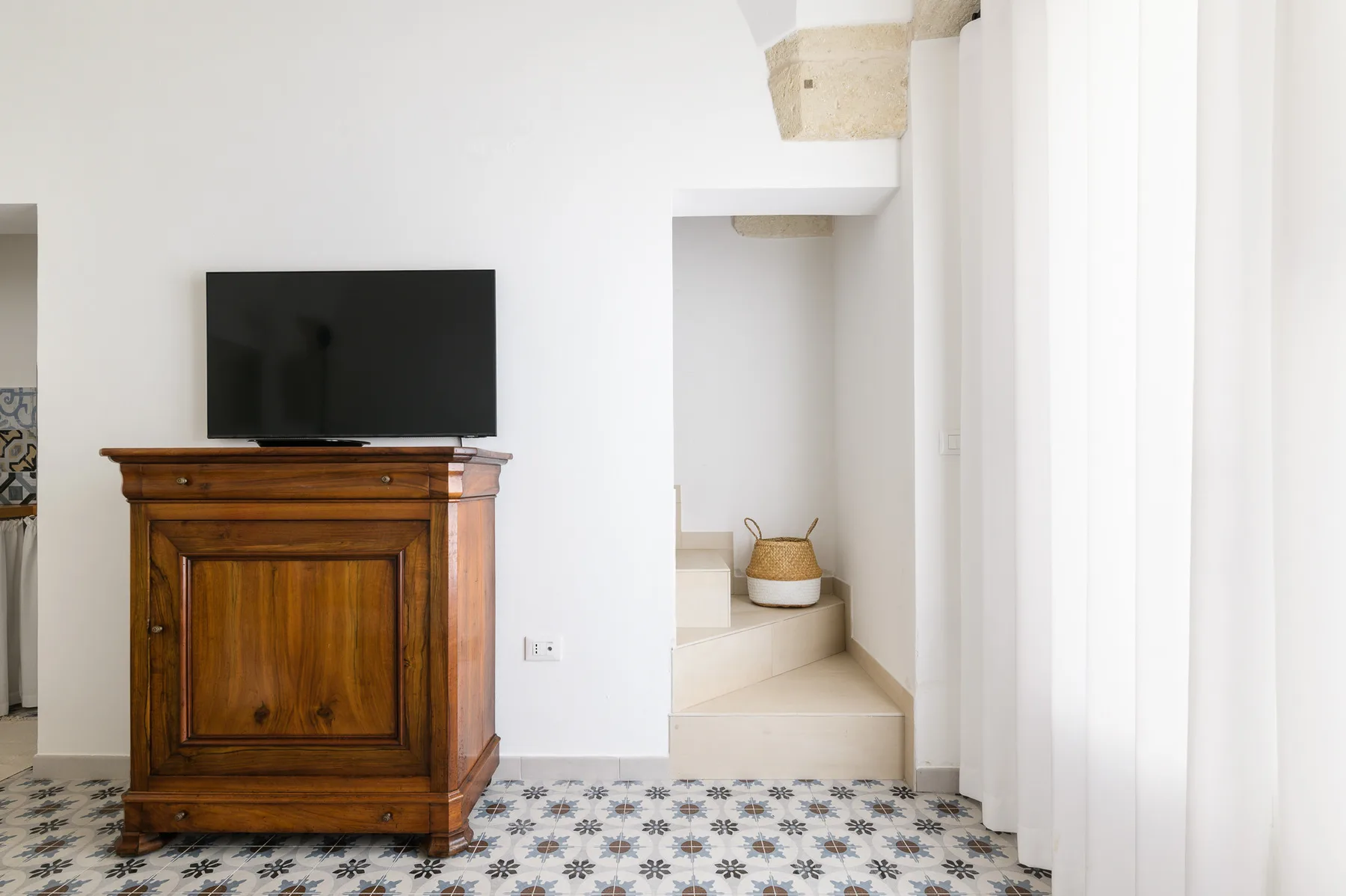 Una habitación luminosa con un mueble de madera y televisor junto a una escalera corta.