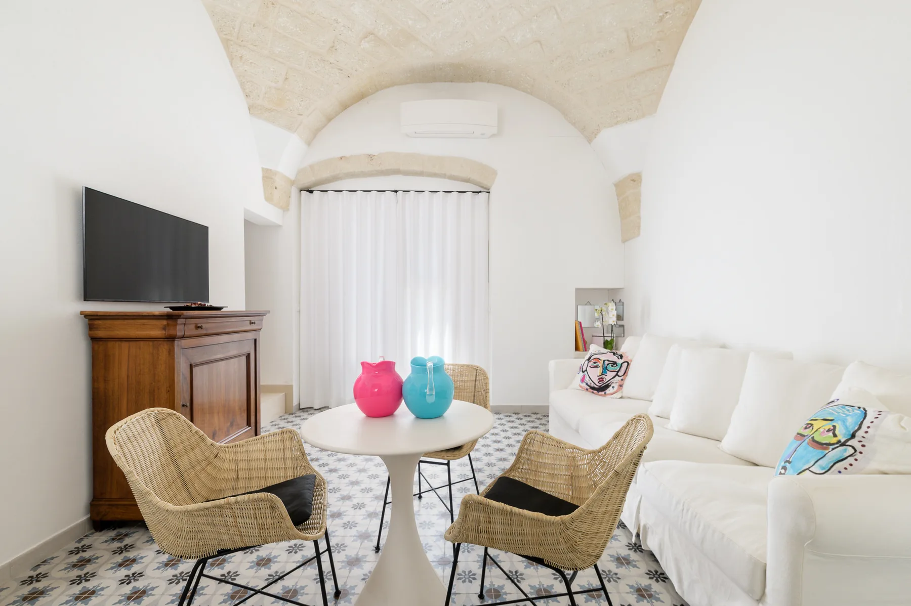 Una sala luminosa con asientos blancos y una mesa redonda entre sillas tejidas.