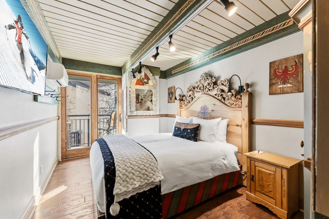 A bedroom with a bed, carved wooden headboard, and glass doors opening onto a balcony.
