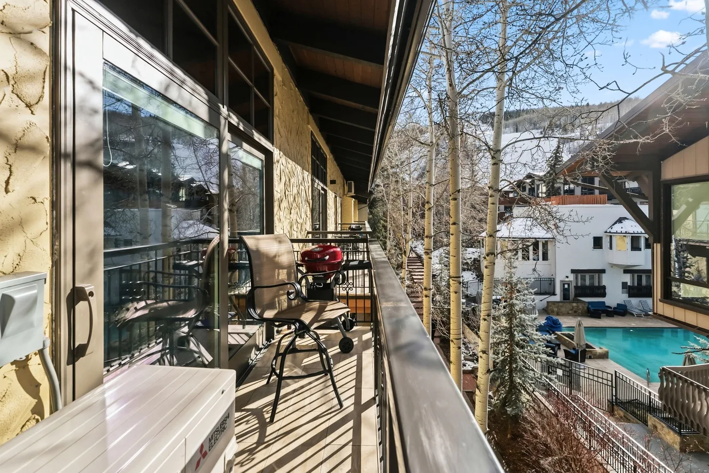 A balcony with outdoor seating overlooks a swimming pool and nearby buildings.