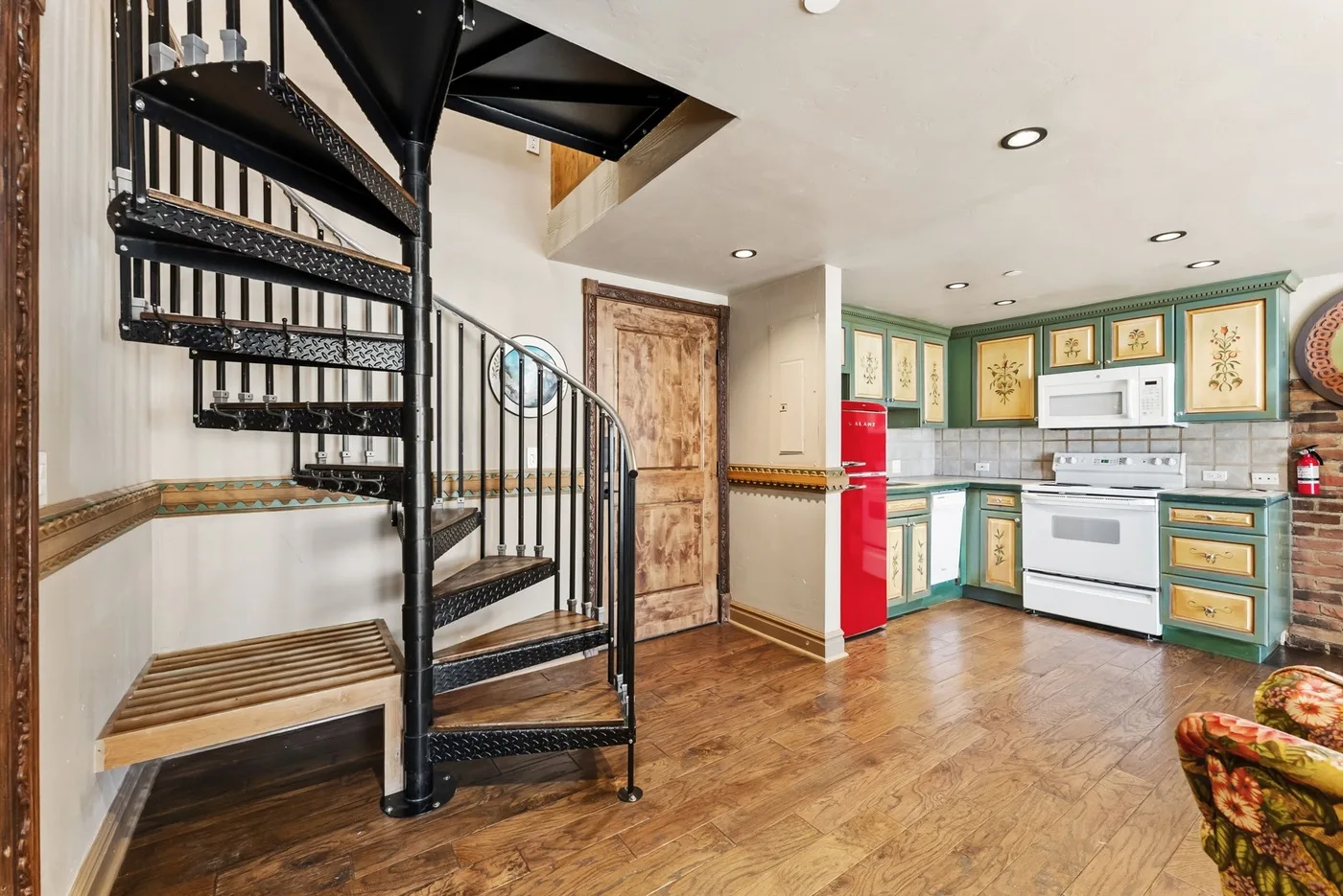 A kitchen with green cabinets, a red refrigerator, and a spiral staircase.