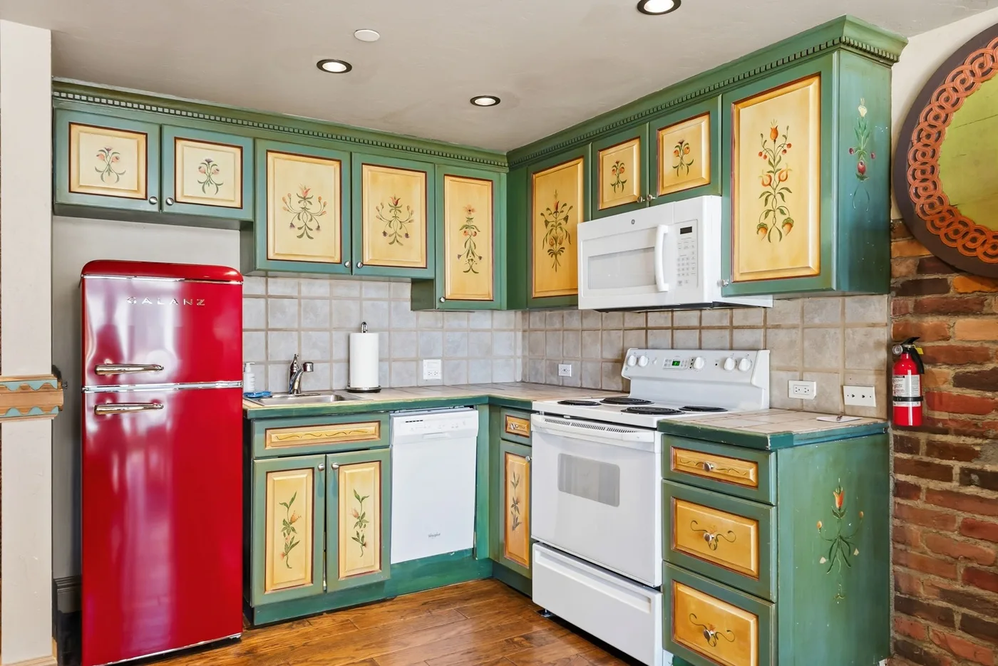 A colorful kitchen with green cabinets, a red refrigerator, and a white stove.