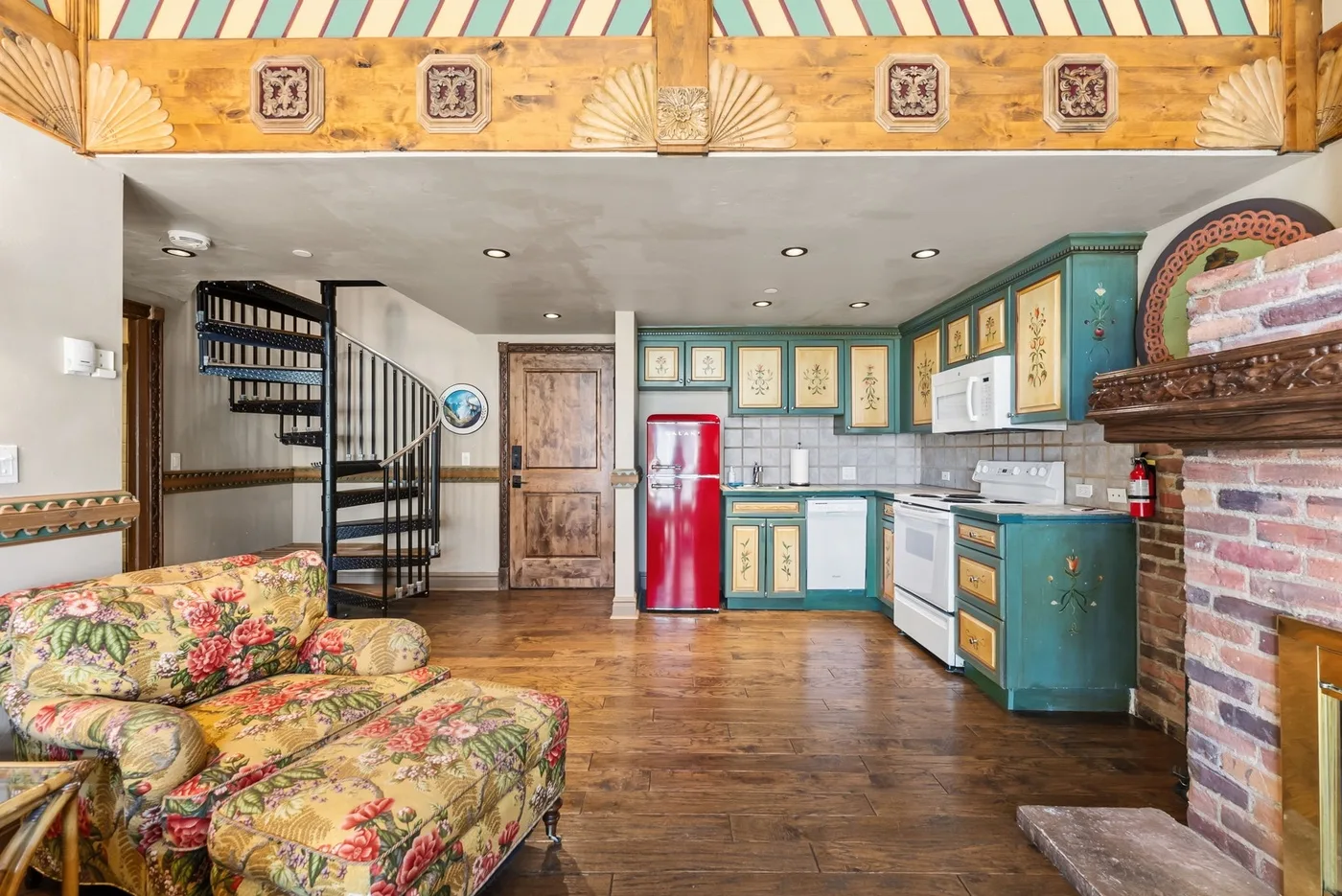 A colorful living room opens onto a kitchen with teal cabinets and a red refrigerator.
