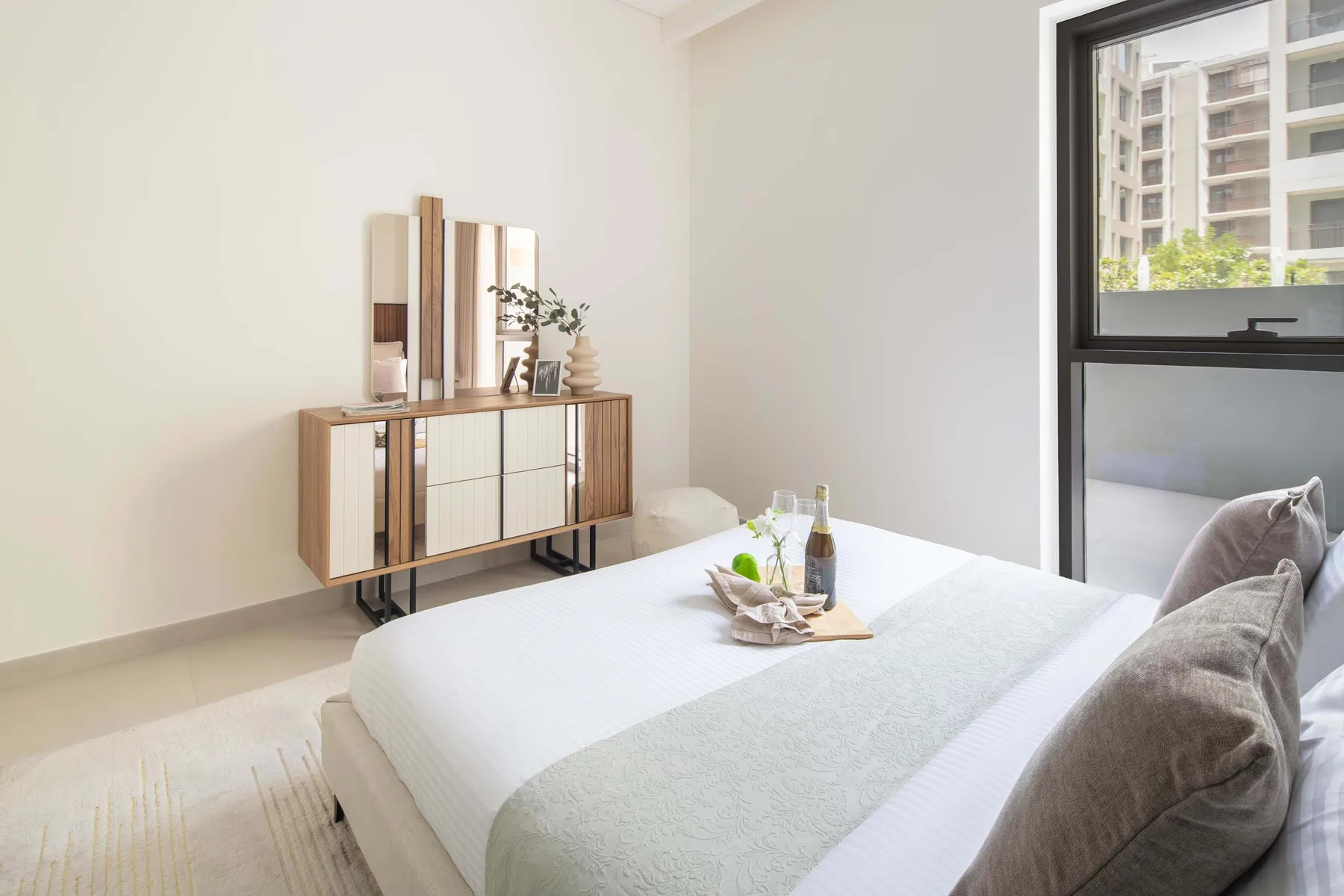 Un dormitorio luminoso con una cama bien arreglada y un aparador de madera.