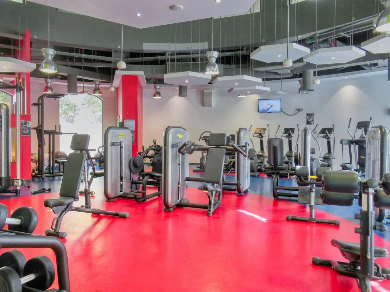 A gym with exercise machines and strength-training equipment on a bright red floor.