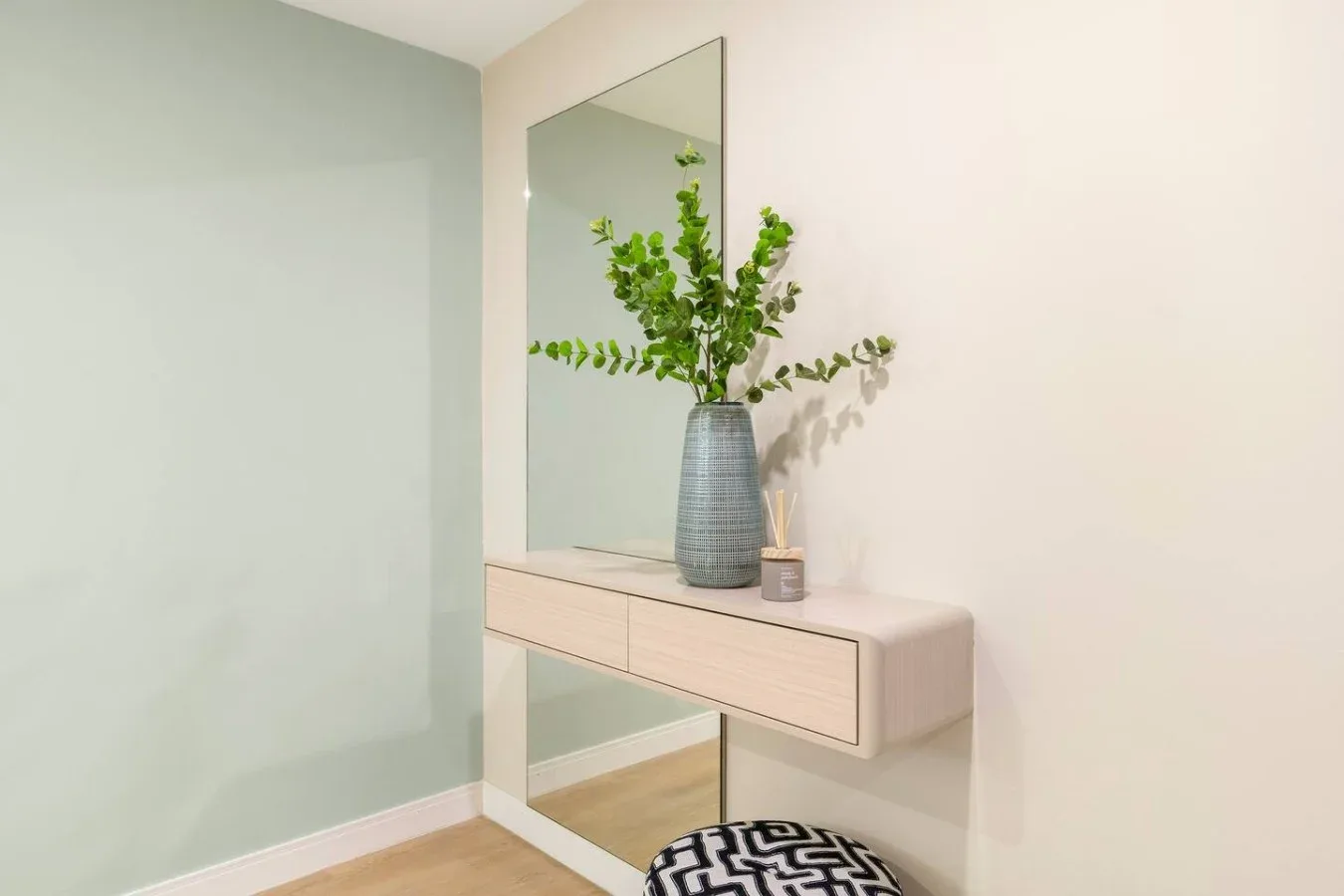 A console table with a vase and greenery stands beneath a wall mirror.