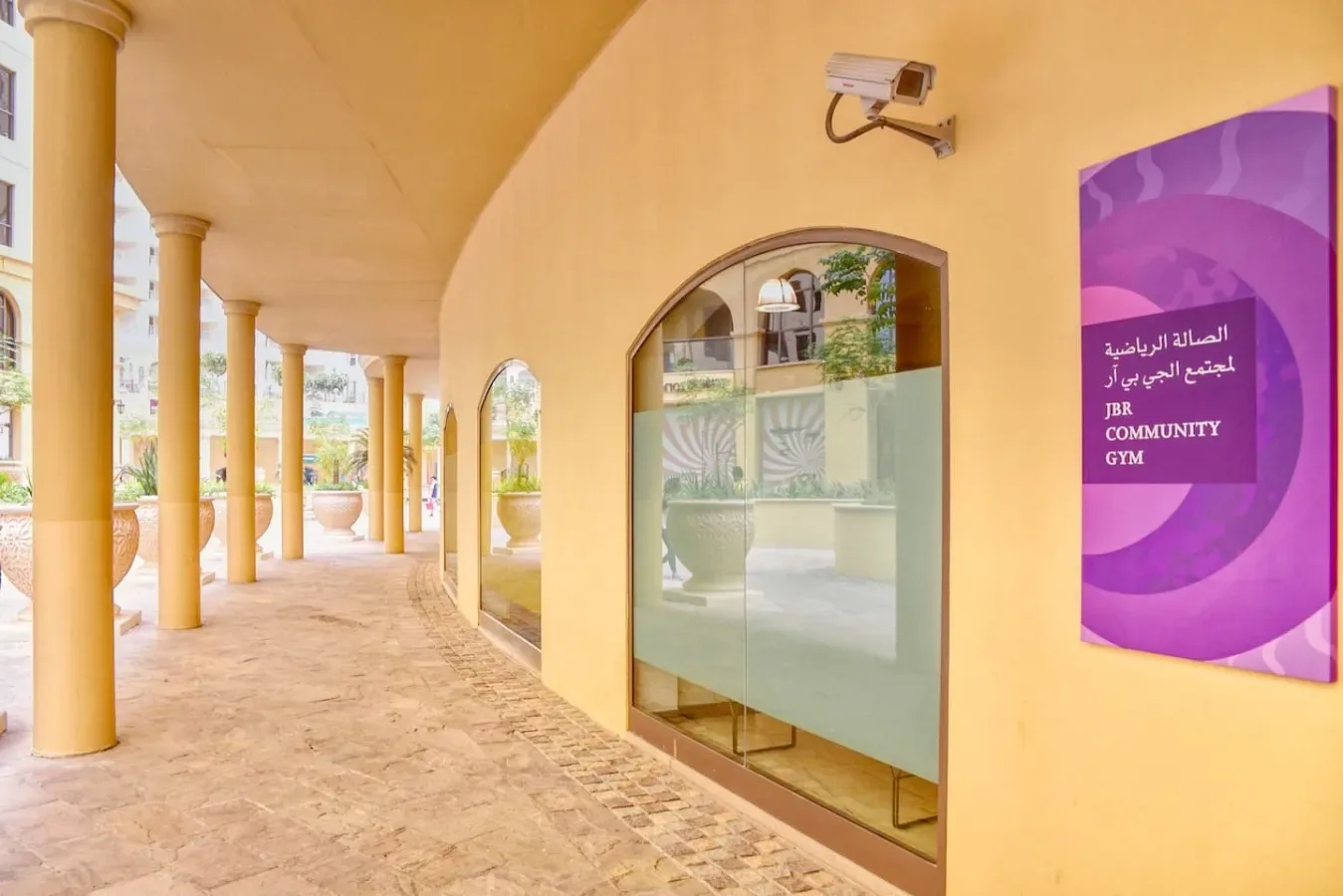 A covered walkway with arched glass doors and a purple community gym sign.