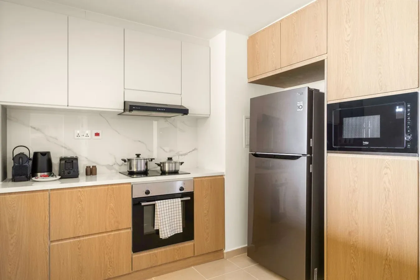 A modern kitchen with light wood cabinets, a refrigerator, and a built-in microwave.