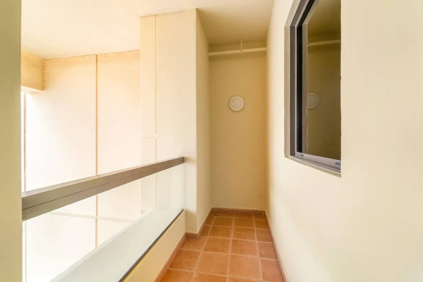 A narrow indoor passage with terracotta-colored floor tiles and a window.