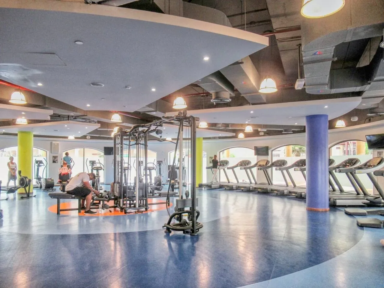 A spacious gym with exercise machines, treadmills, and people working out.