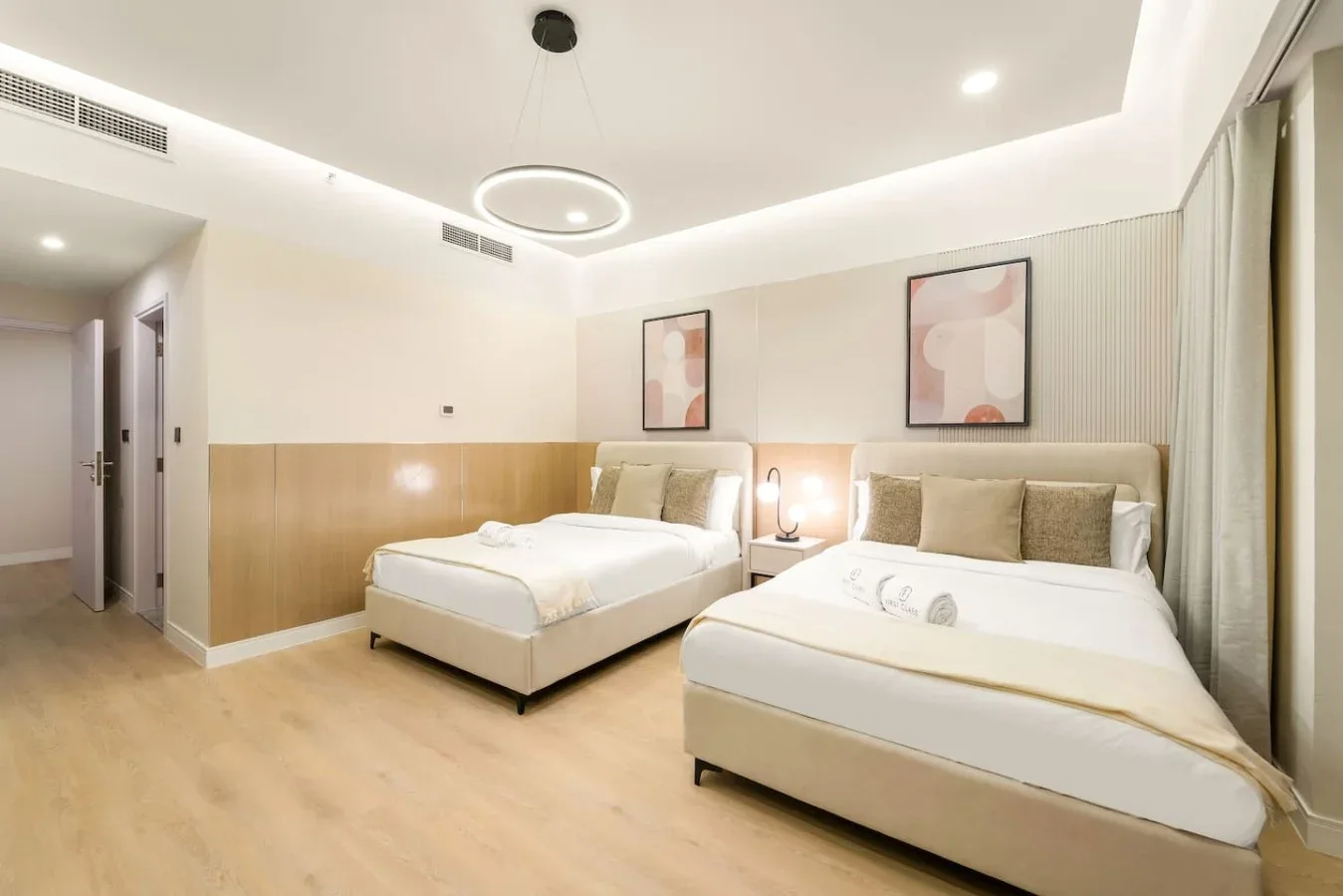 A bright bedroom with two beds, bedside lamps, and abstract wall art.