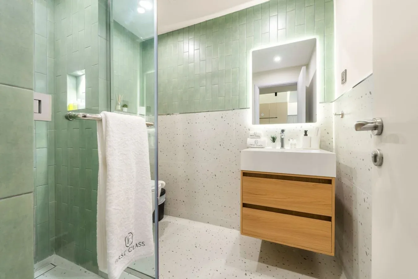 A tiled bathroom with a glass shower, a sink vanity, and a wall mirror.