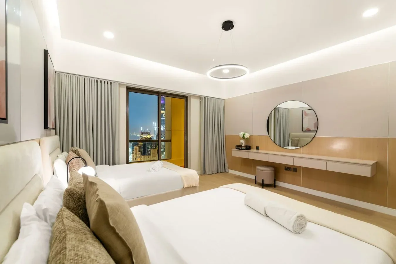 A bright bedroom with two beds and a large window overlooking city lights.