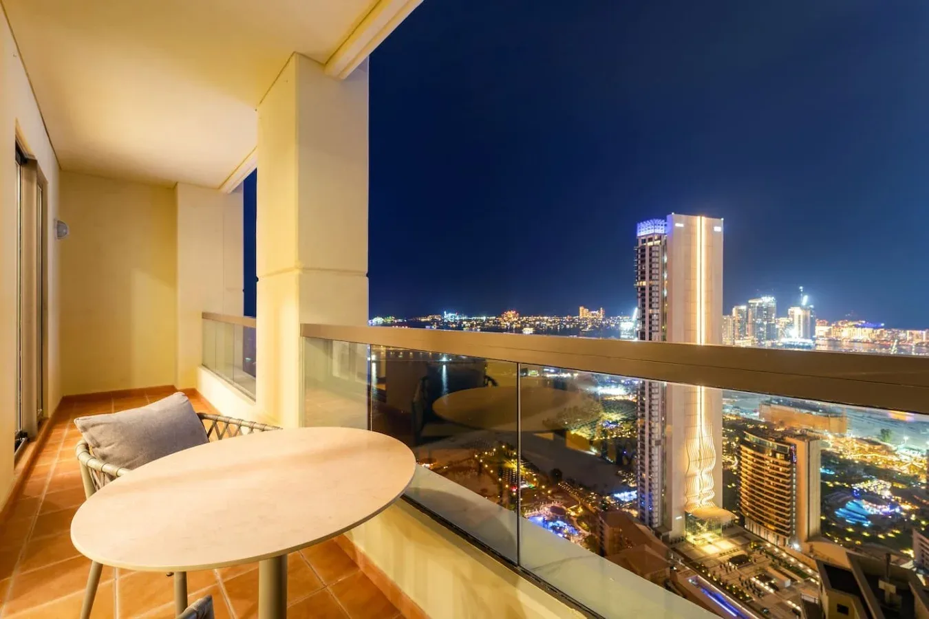 A balcony seating area overlooks a brightly lit city skyline at night.