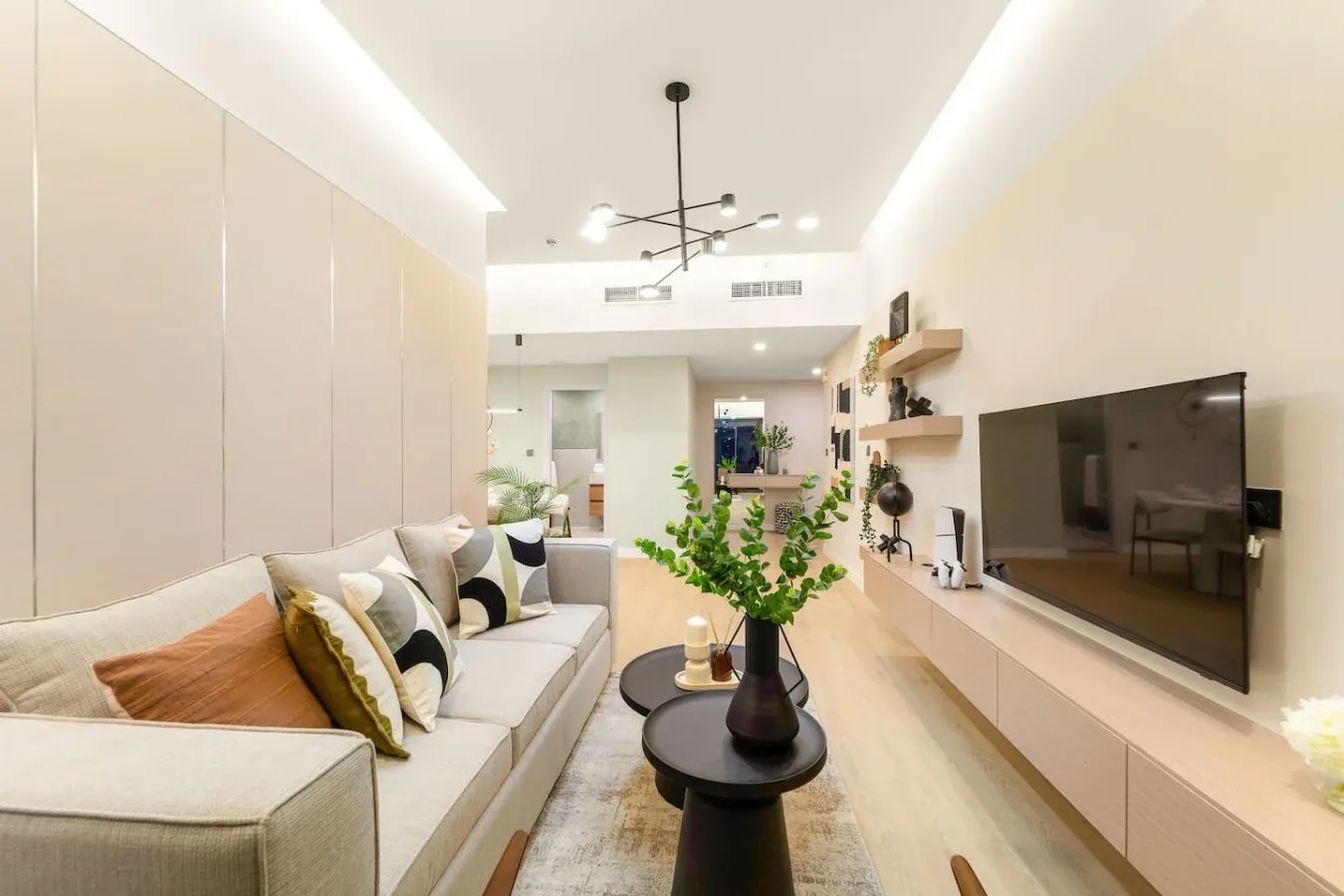 A bright living room with a light-colored seating area and television.