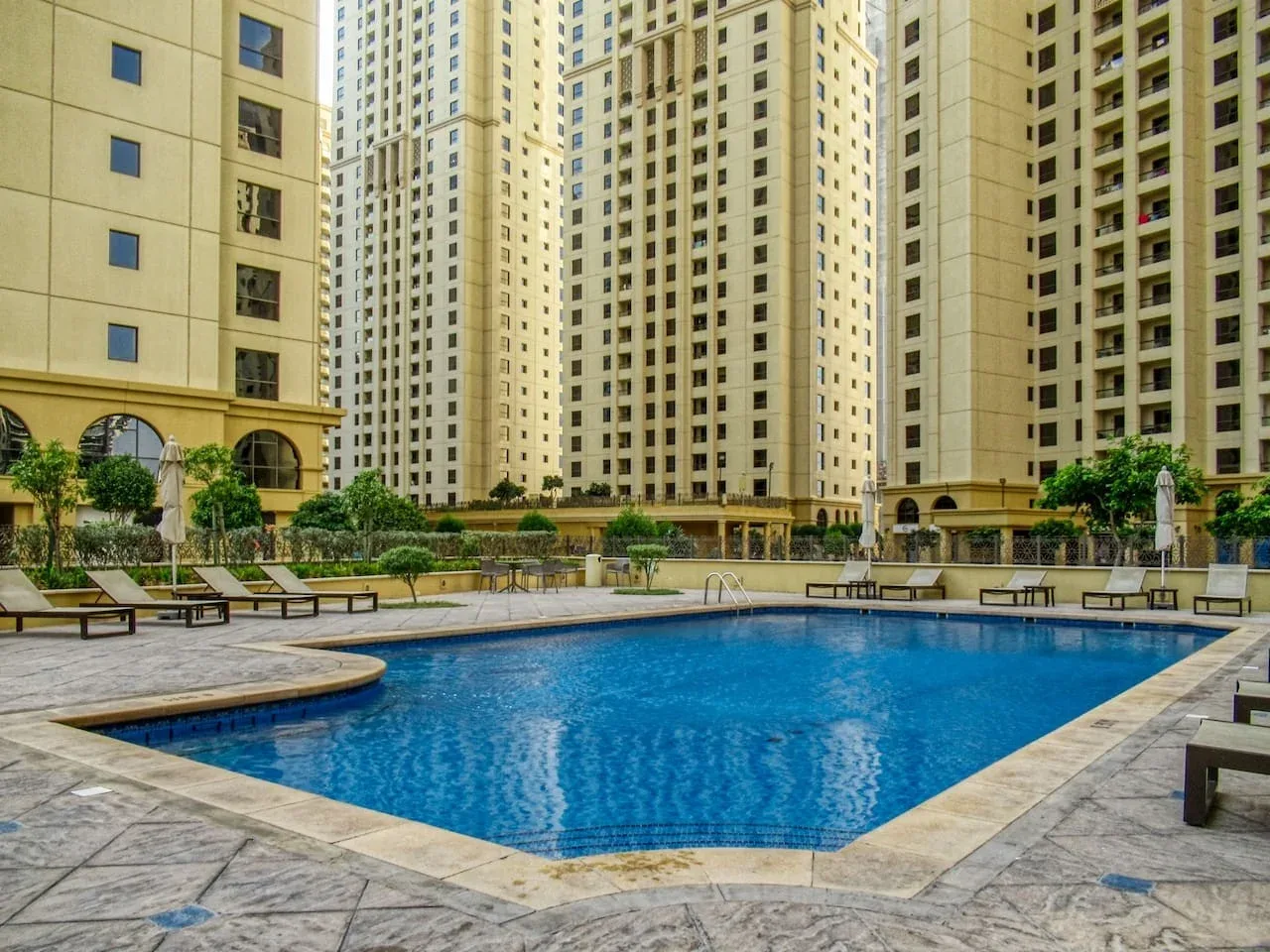 A swimming pool sits in a paved courtyard surrounded by tall apartment buildings.