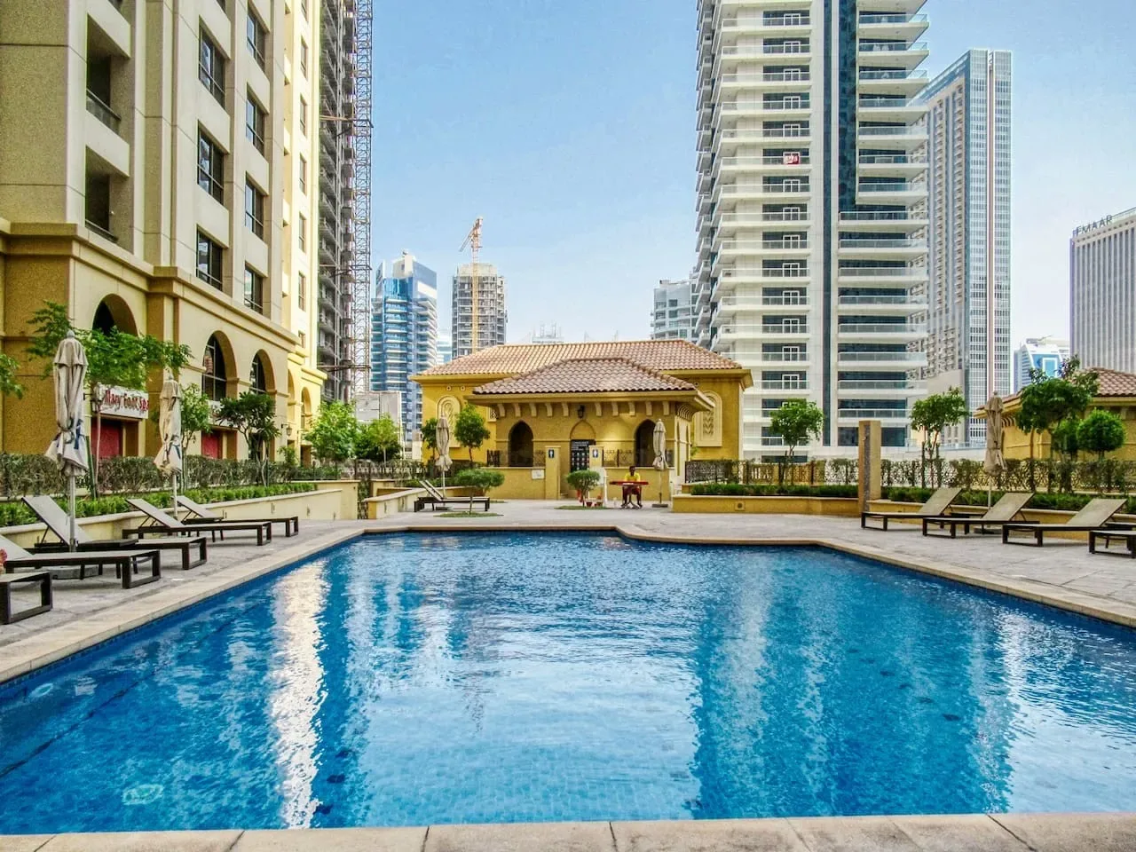 Una piscina al aire libre está rodeada de edificios altos, con un edificio bajo al fondo.