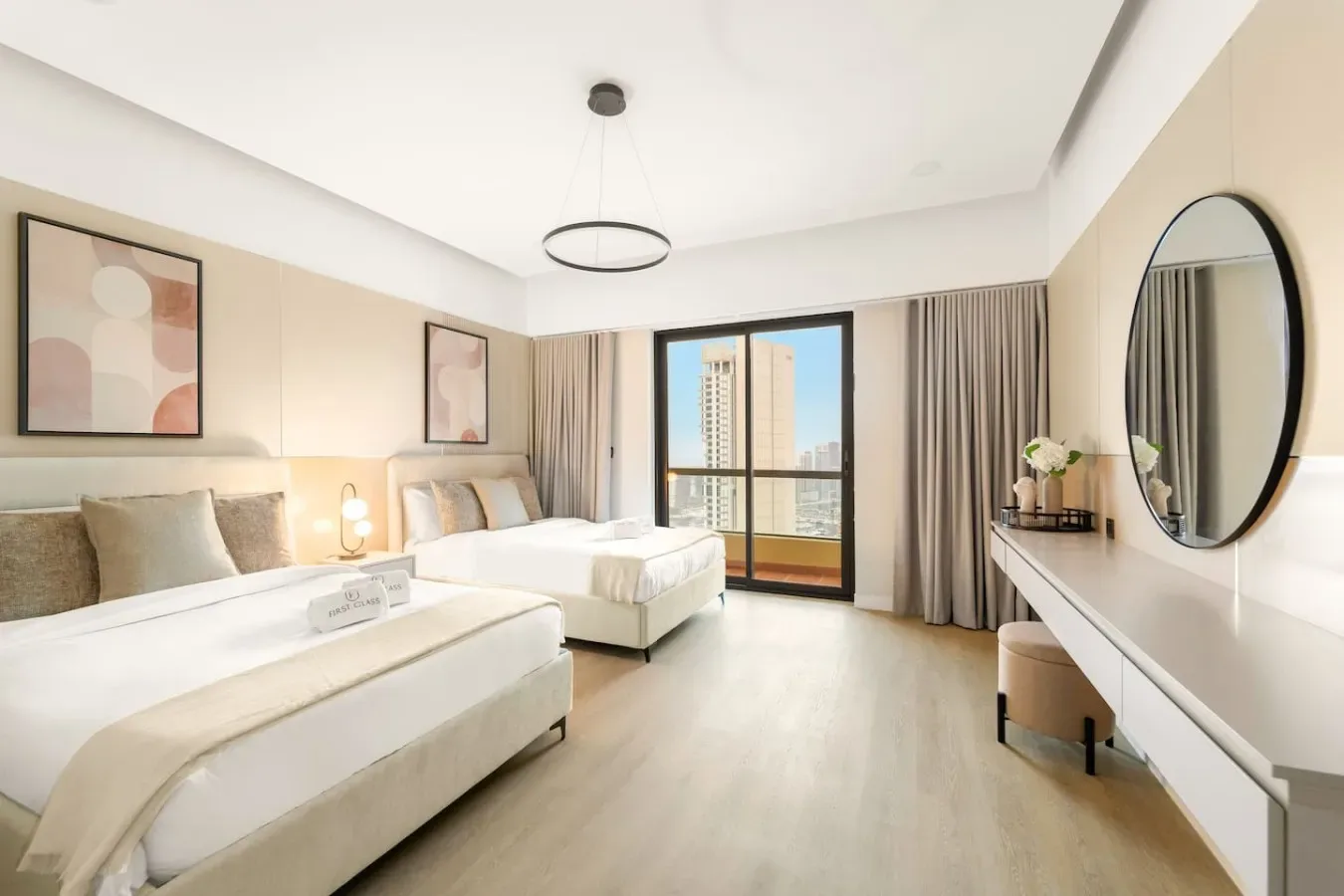 A bright bedroom with two beds, a large window, and a dressing table.