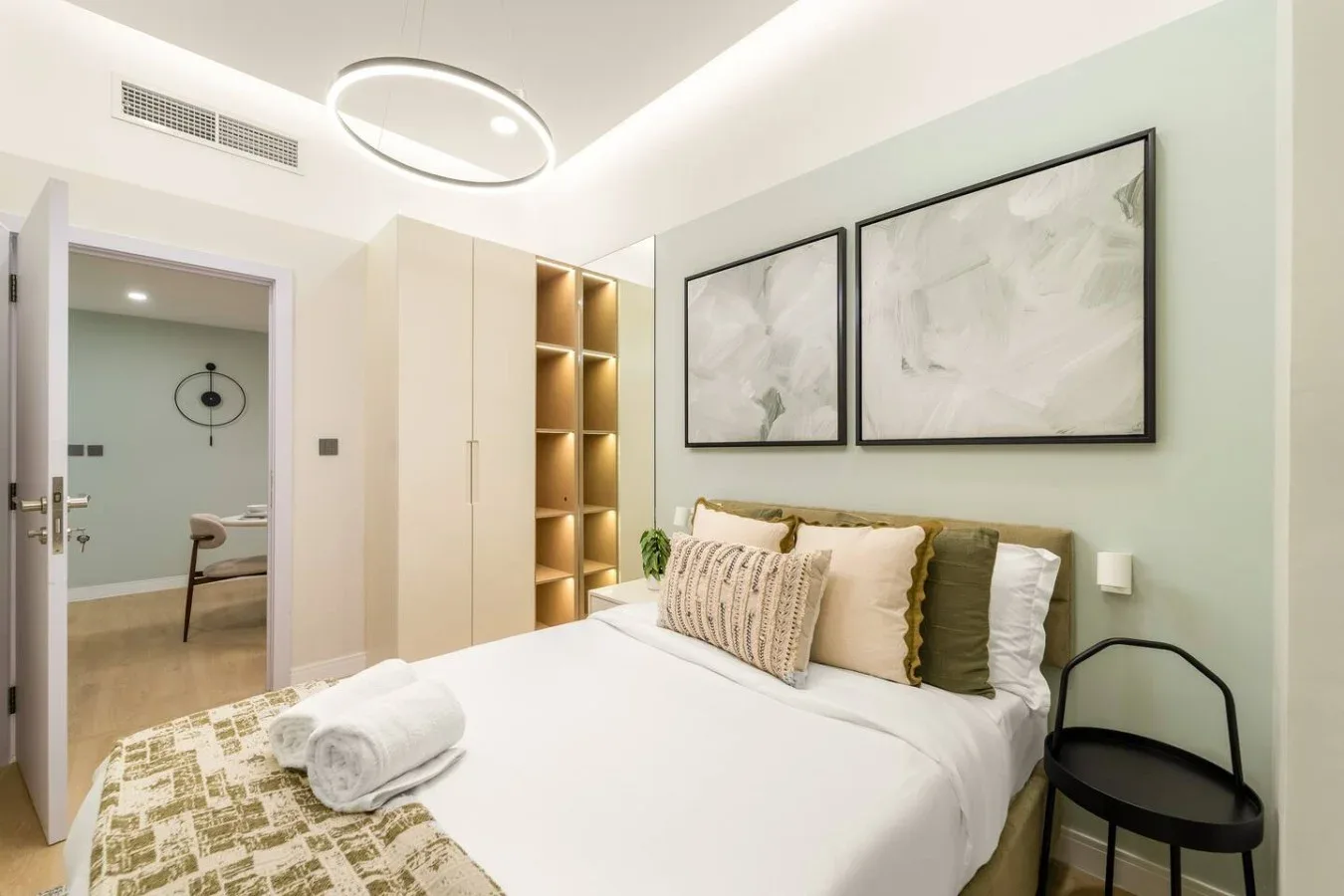 A bright bedroom with a neatly made bed and framed artwork above it.