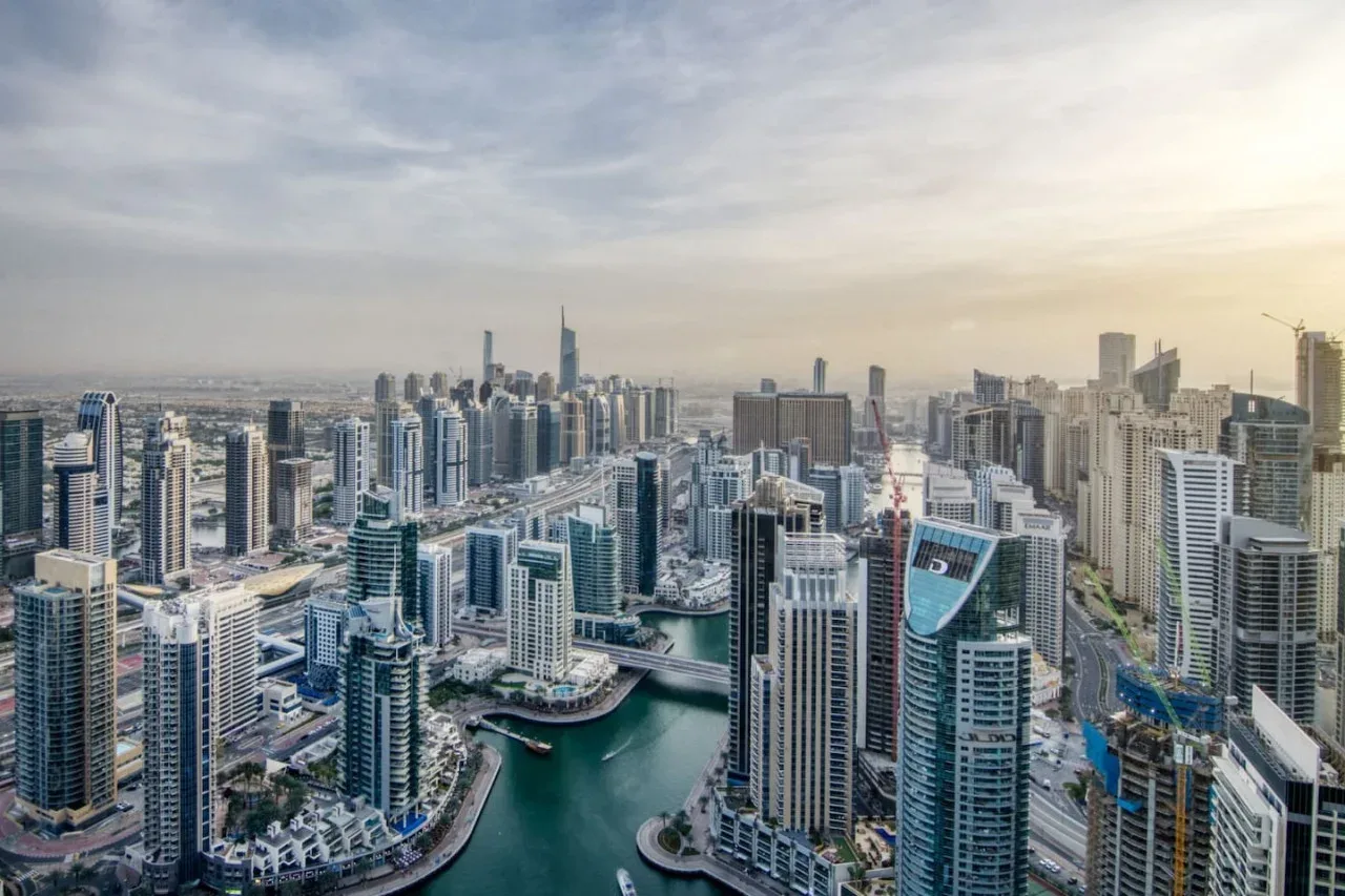 A panoramic city skyline of high-rise buildings surrounding a marina.