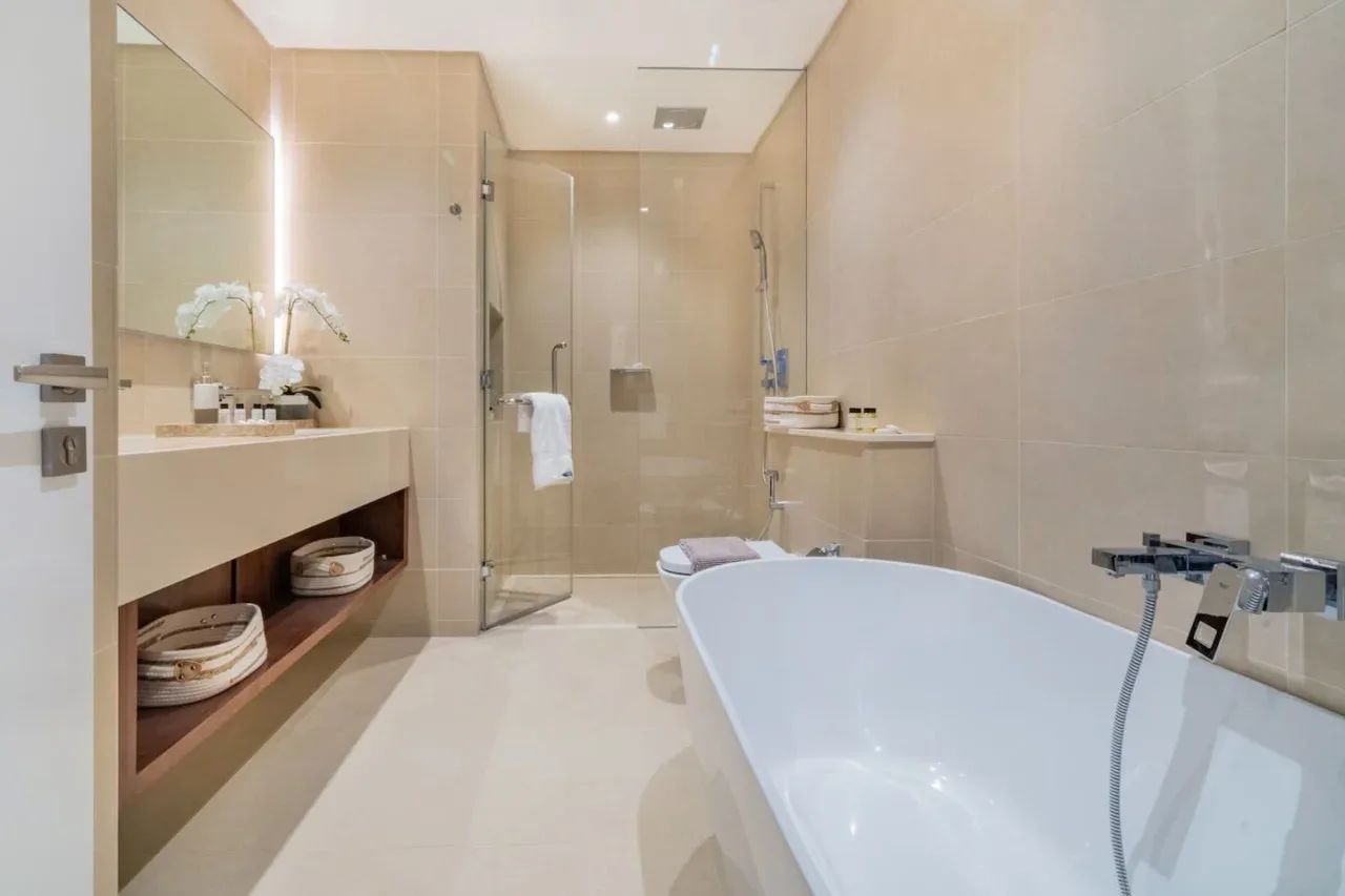A spacious bathroom with a bathtub, glass shower, and pale tile.