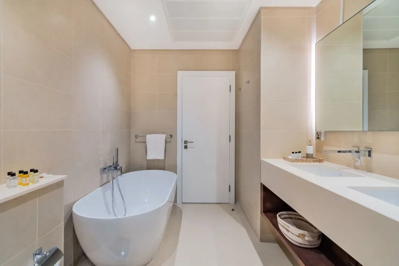 A tiled bathroom with a bathtub, towel rail, and long vanity.