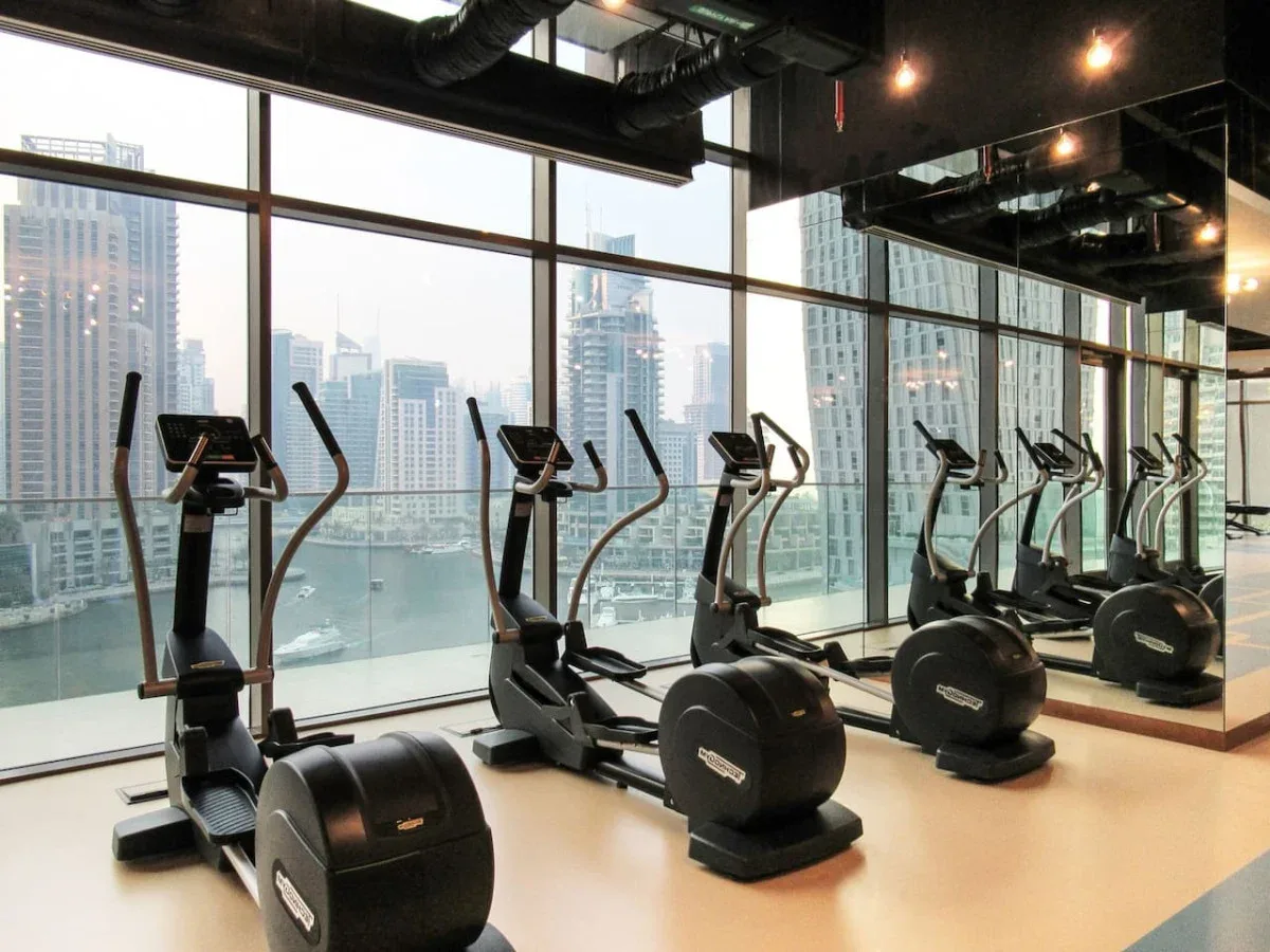 A fitness room with exercise machines beside floor-to-ceiling windows.